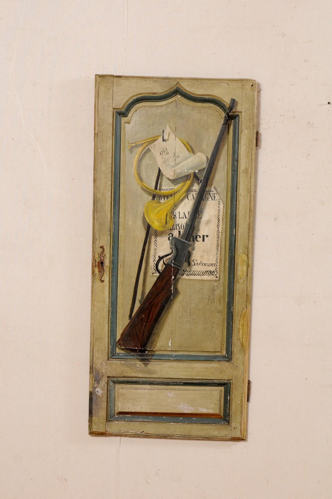 A French trompe l'oeil door from the 19th century. This single antique door from France, with its shorter 4.5 foot (approximate) height, features a trompe l'oeil painted finish is a hunters motif (complete with French horn and riffle). The raised
