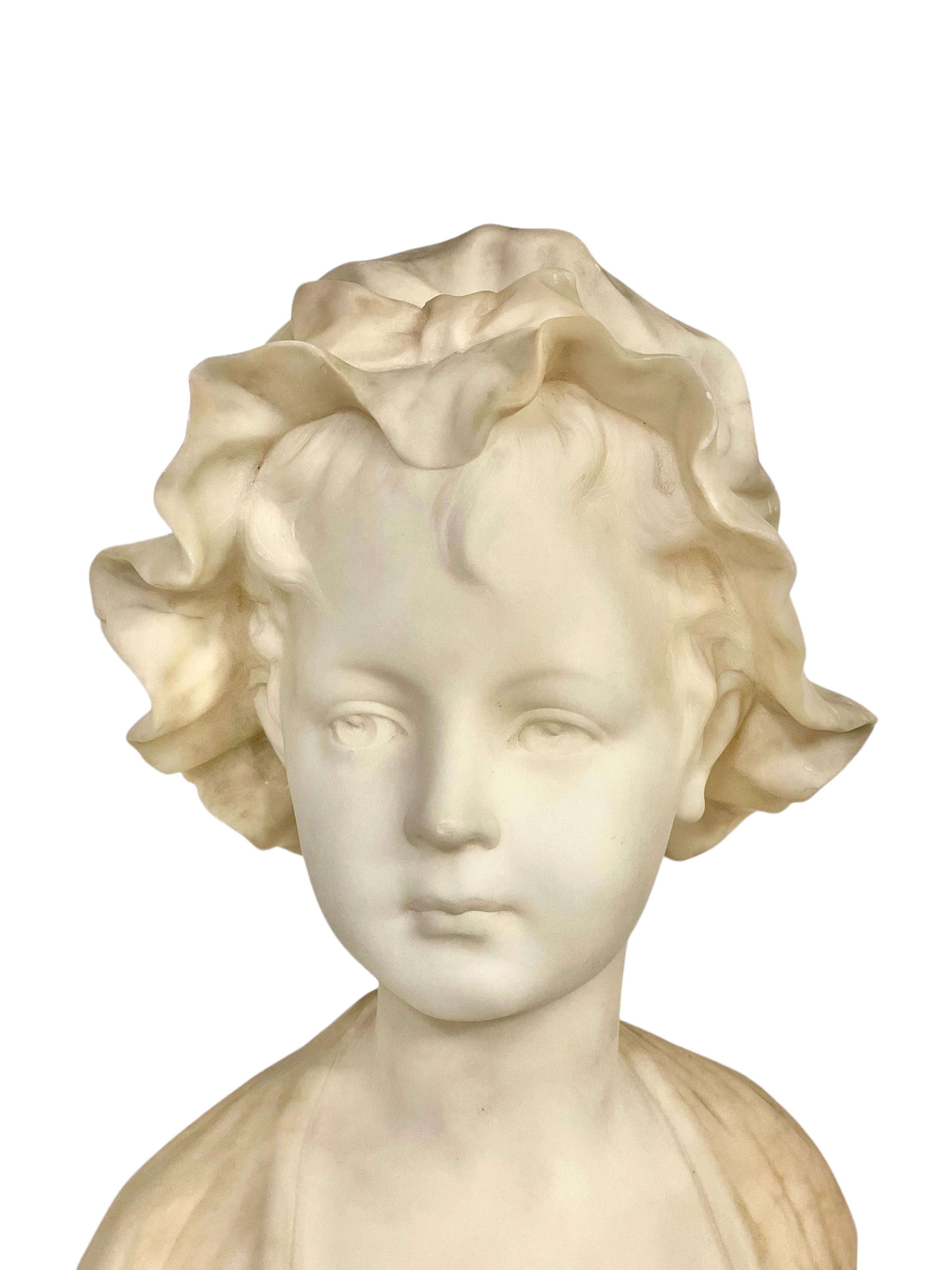 This 19th-century alabaster bust portrays a charming young girl with an exquisite profile. The statue, crafted in a pristine white hue, captures the innocence and grace of youth. The intricately veined gray bonnet, crowned with a neatly tied bow,
