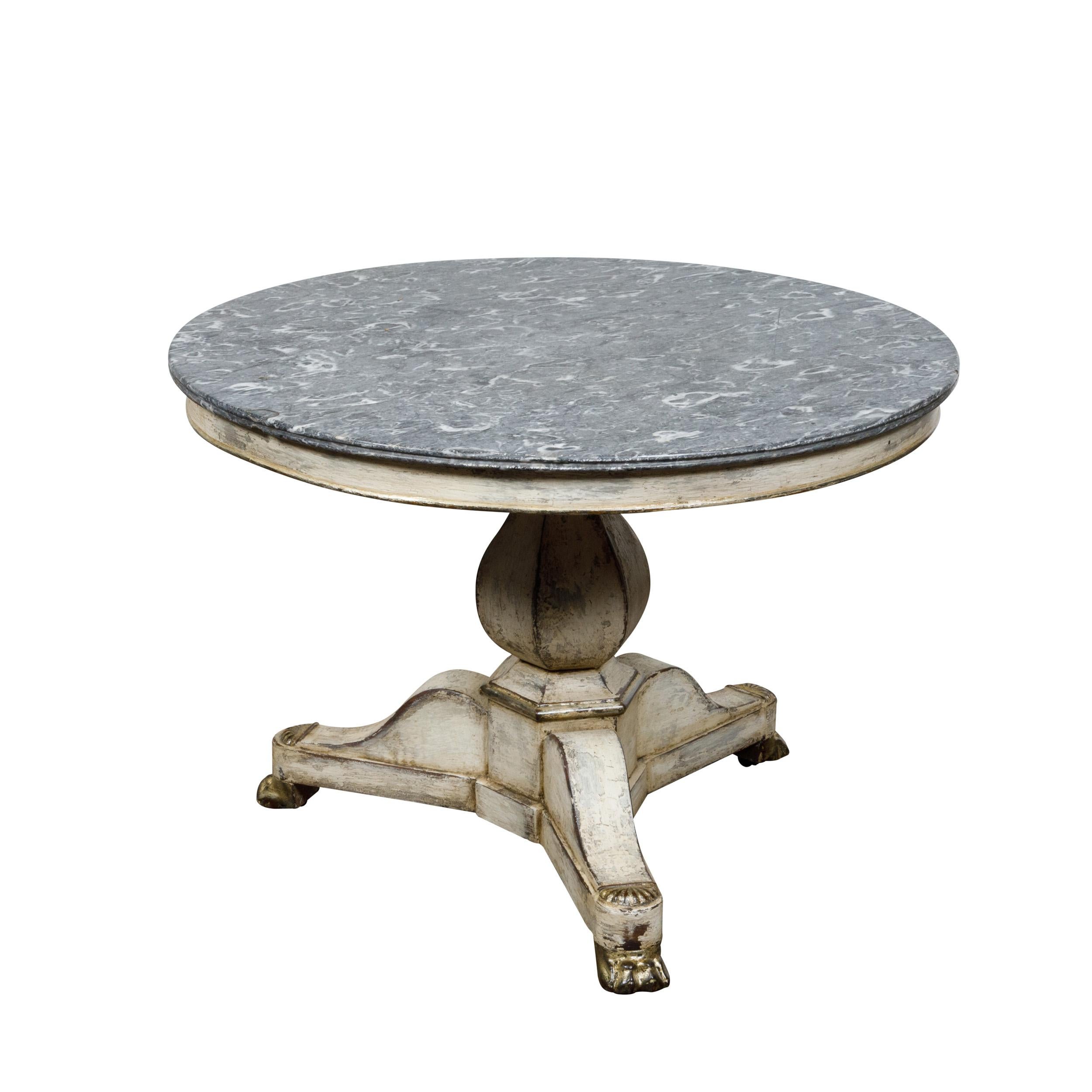 A French antique white painted table from the 19th century with circular variegated gray marble top, bulbous pedestal on tripartite base with carved giltwood lion paw feet. This French antique table, dating back to the 19th century, exudes a