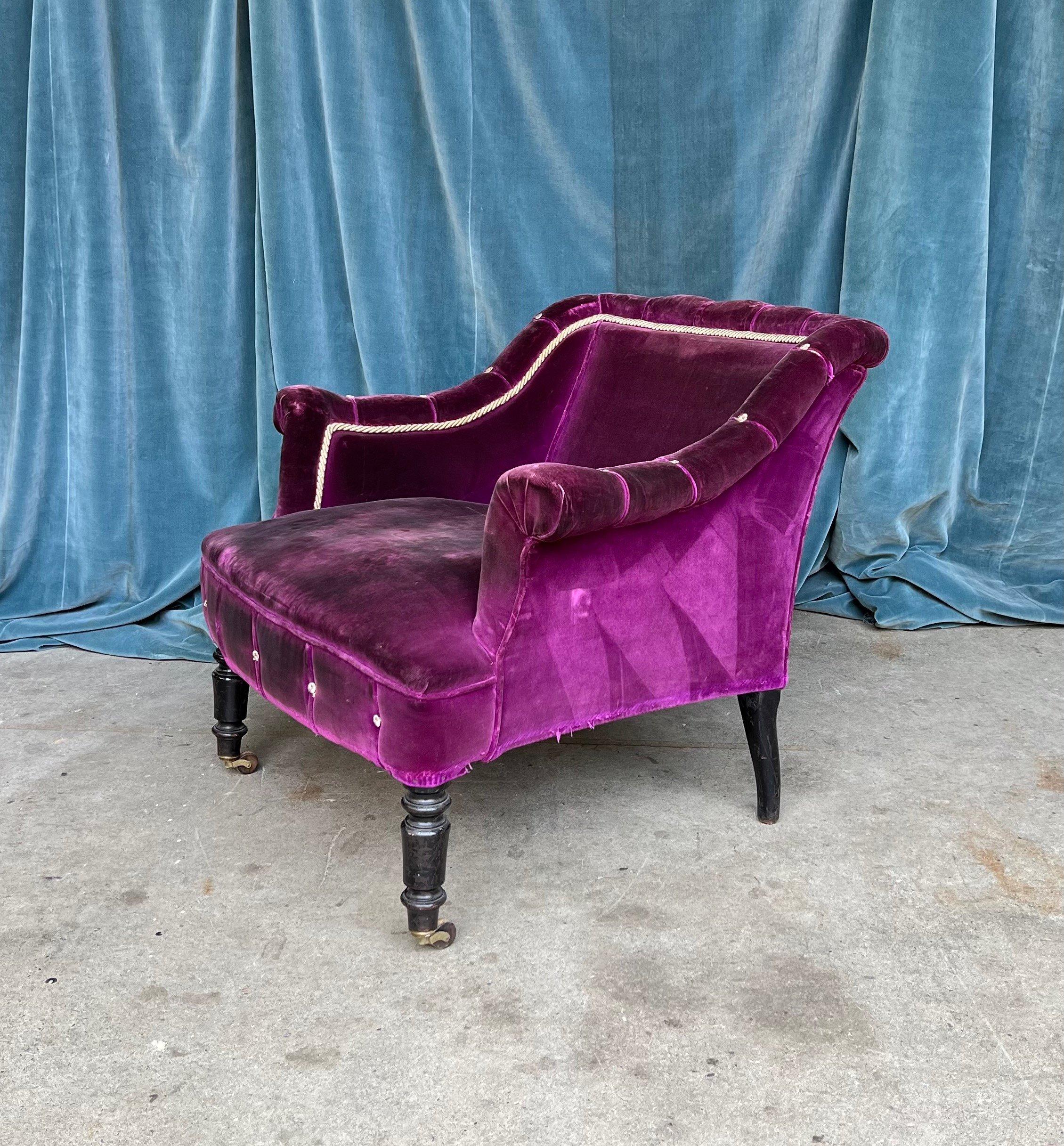 A captivating French 19th century distressed purple velvet armchair. Crafted in 19th century France, in the distinctive Napoleon III style, this armchair is elegant and timeless. It features low bankrolled arms, white braiding and buttons, and