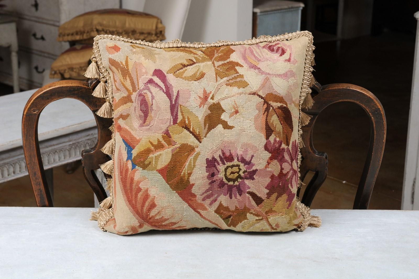 A French Aubusson tapestry pillow from the 19th century, with floral decor and petite tassels. Created during the 19th century in the Aubusson tapestry manufacture located in central France, this pillow features eye-catching pink and purple roses