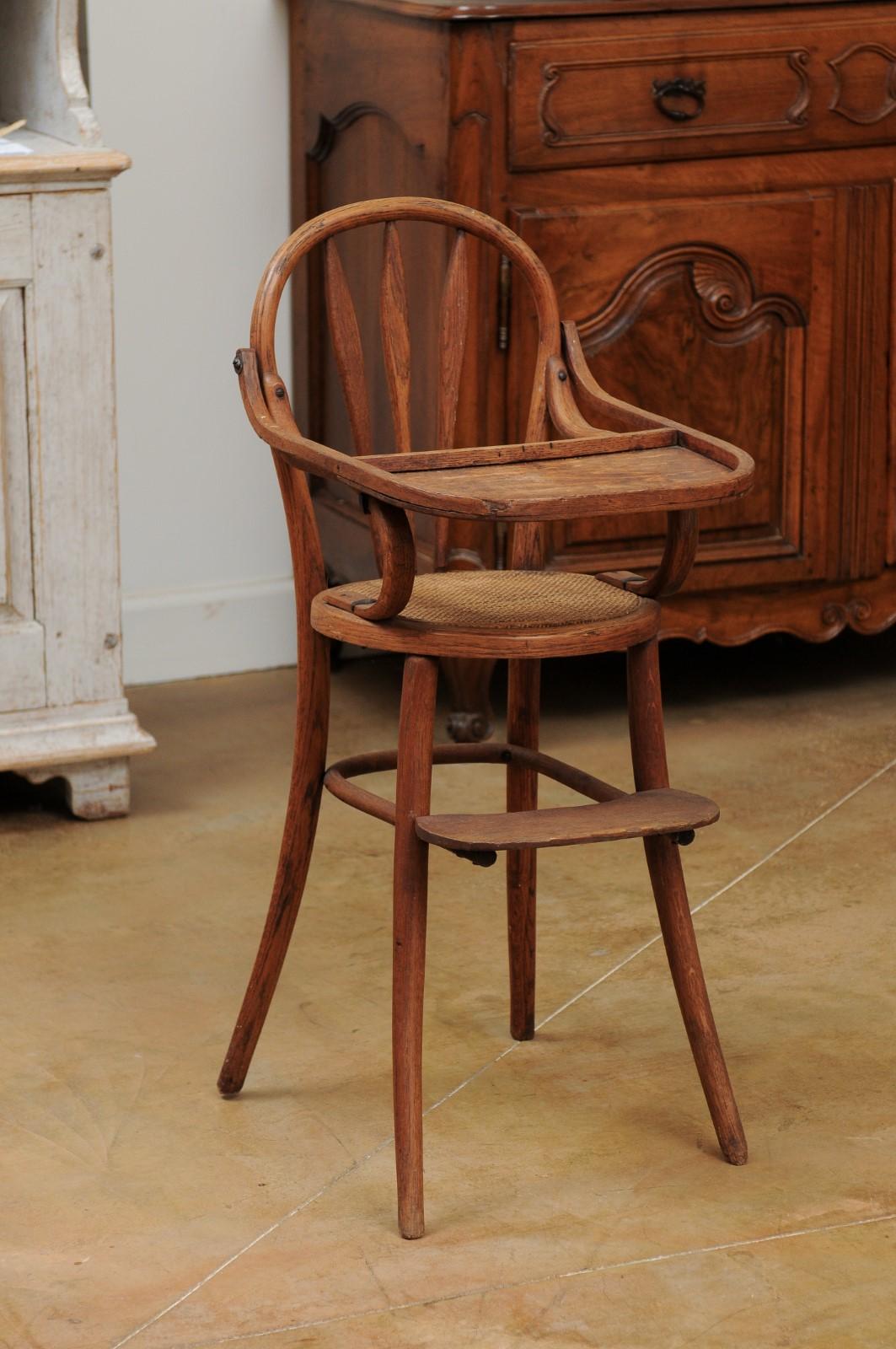 A French baby's high chair from the 19th century, with cane seat and weathered patina. Created in France during the 19th century, this high chair charms us with its rustic appeal and grand simplicity. The curving backrest is connected to two simply