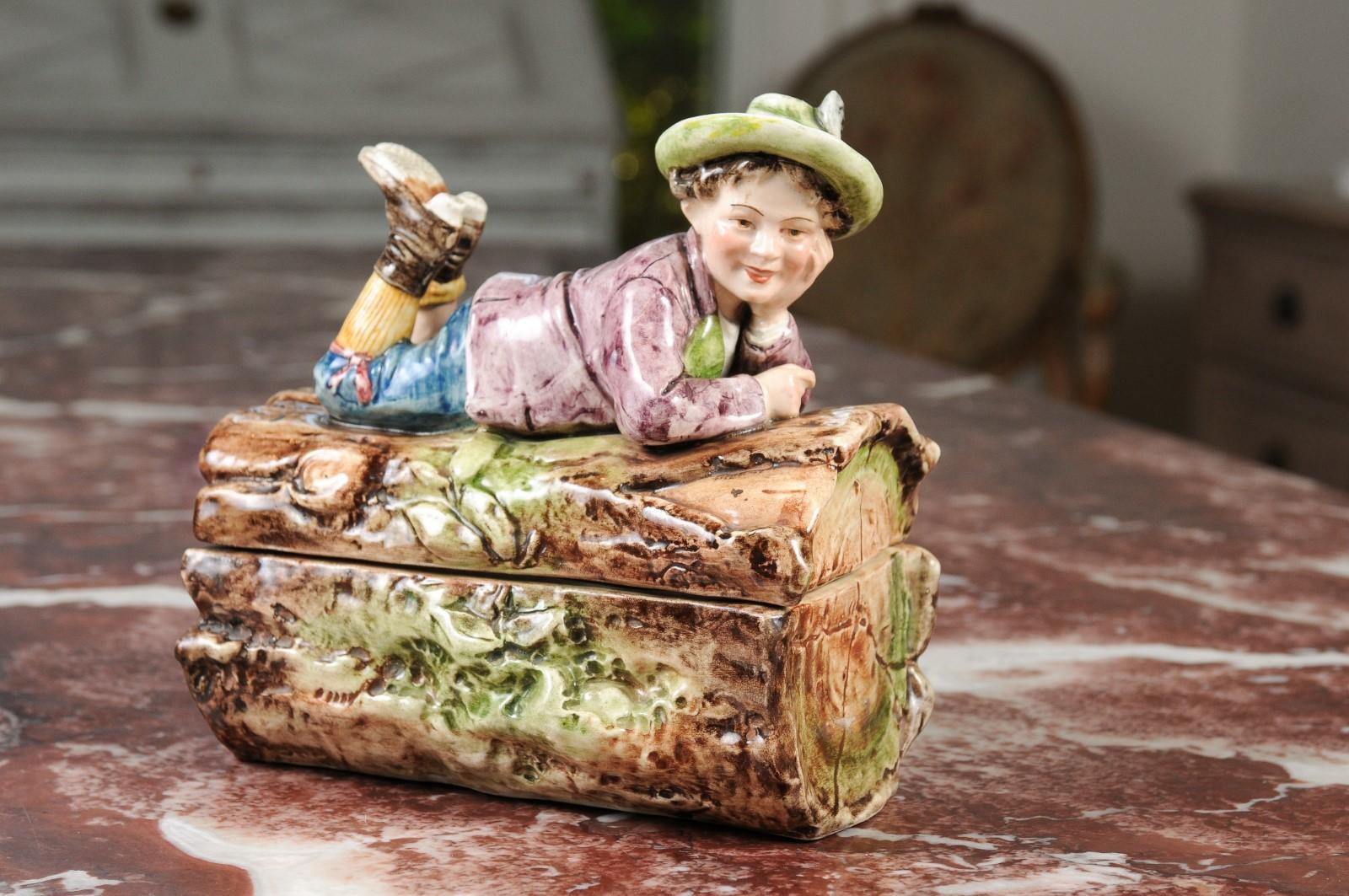 Eine französische Barbotine-Bonbondose aus dem 19. Jahrhundert, die einen Jungen darstellt, der auf einem Baumstamm liegt. Diese bezaubernde Bonbondose stammt aus dem Frankreich des 19. Jahrhunderts und zeigt ein zartes Barbotine-Dekor, das eine