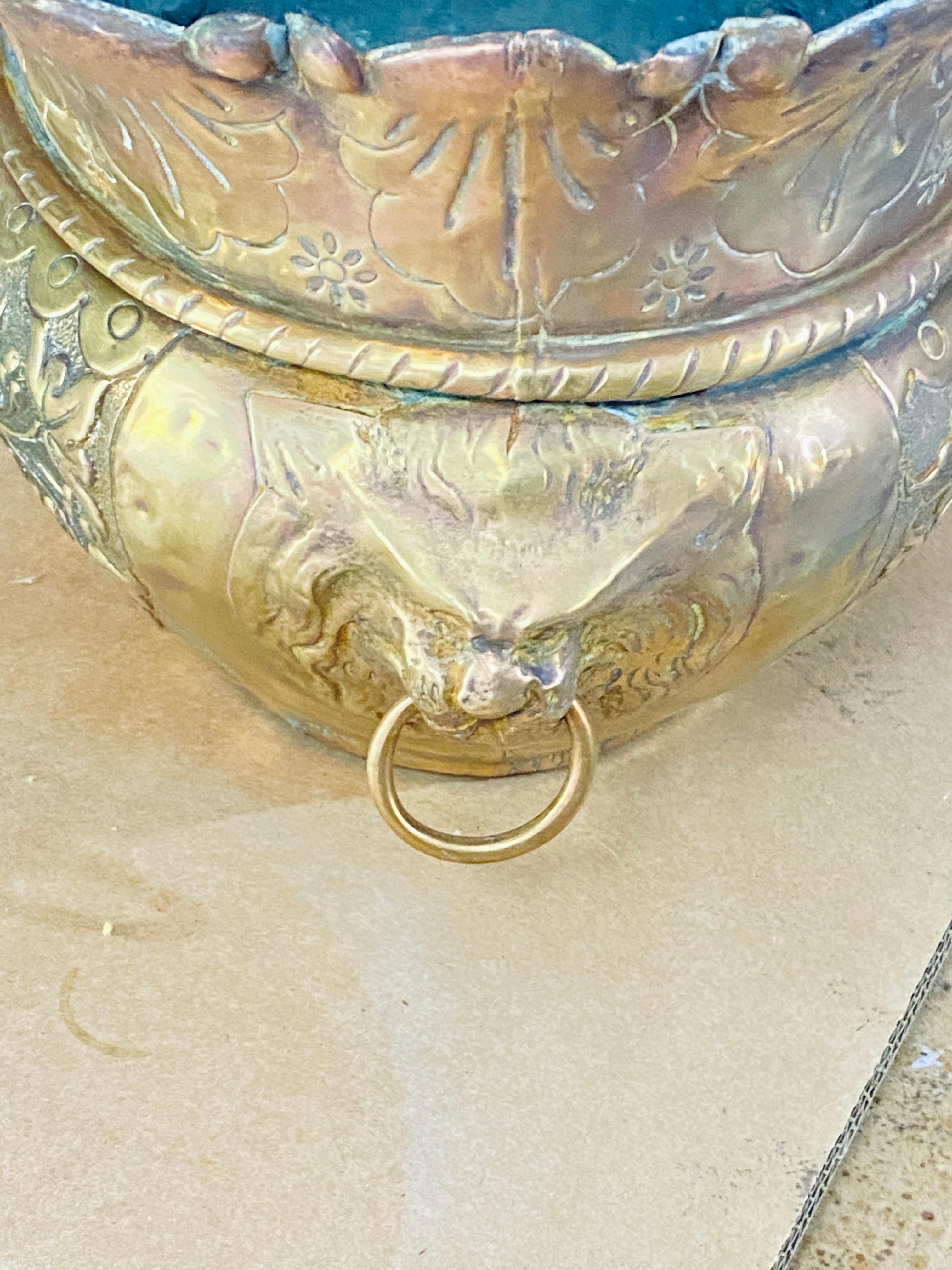 19th century French brass planter. The color is golden, and we have lion heads in decorative motifs. It's a rather baroque decor, which reveals the old patina of the brass.
