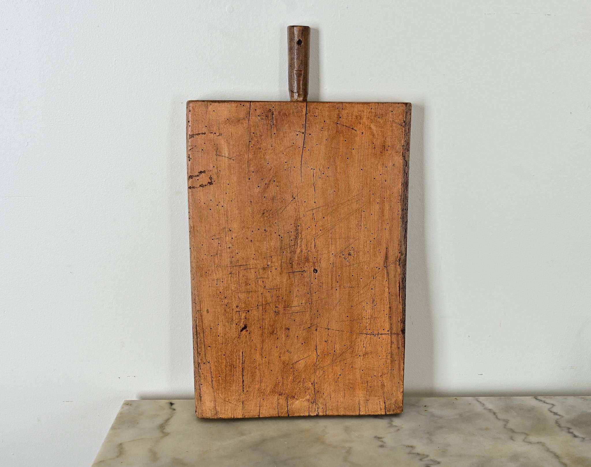 Cette planche à découper en hêtre massif est dotée d'une poignée improvisée en goujon cylindrique sculpté à la main et fixé au sommet par un clou en métal. Une préférence nette pour l'utilisation d'un côté de la planche est attestée par un groupe