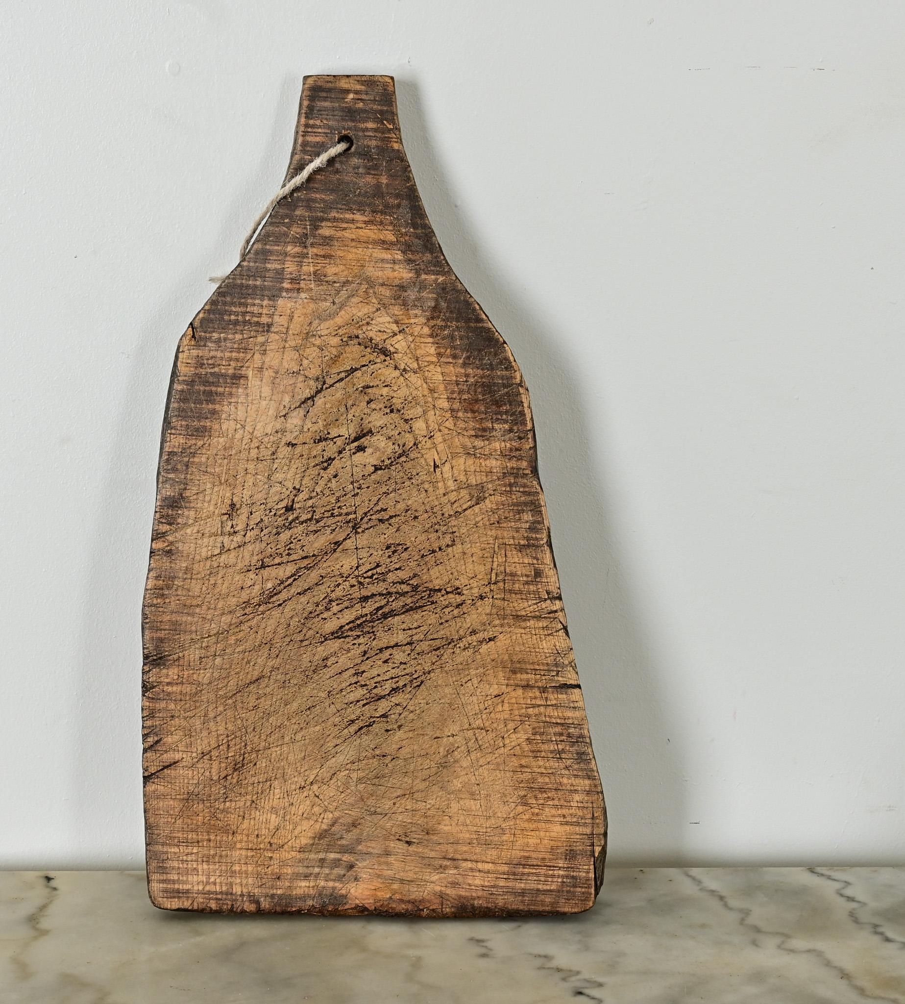 Fraisée et sculptée dans une section massive de bois de hêtre, cette planche à découper datant de la France du XIXe siècle porte encore les ondulations d'un bord vivant où l'écorce a été perdue. Les deux faces de la planche massive sont incisées de