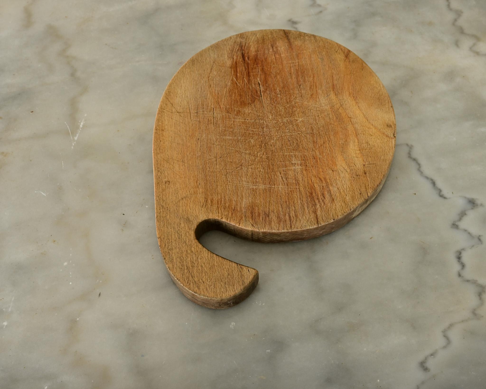 Une planche à découper en bois massif de France de forme ronde avec une poignée de forme intéressante. La planche usée est faite d'une seule pièce de bois avec des marques de couteau et des dépressions sur les deux côtés. Une belle antiquité, pleine