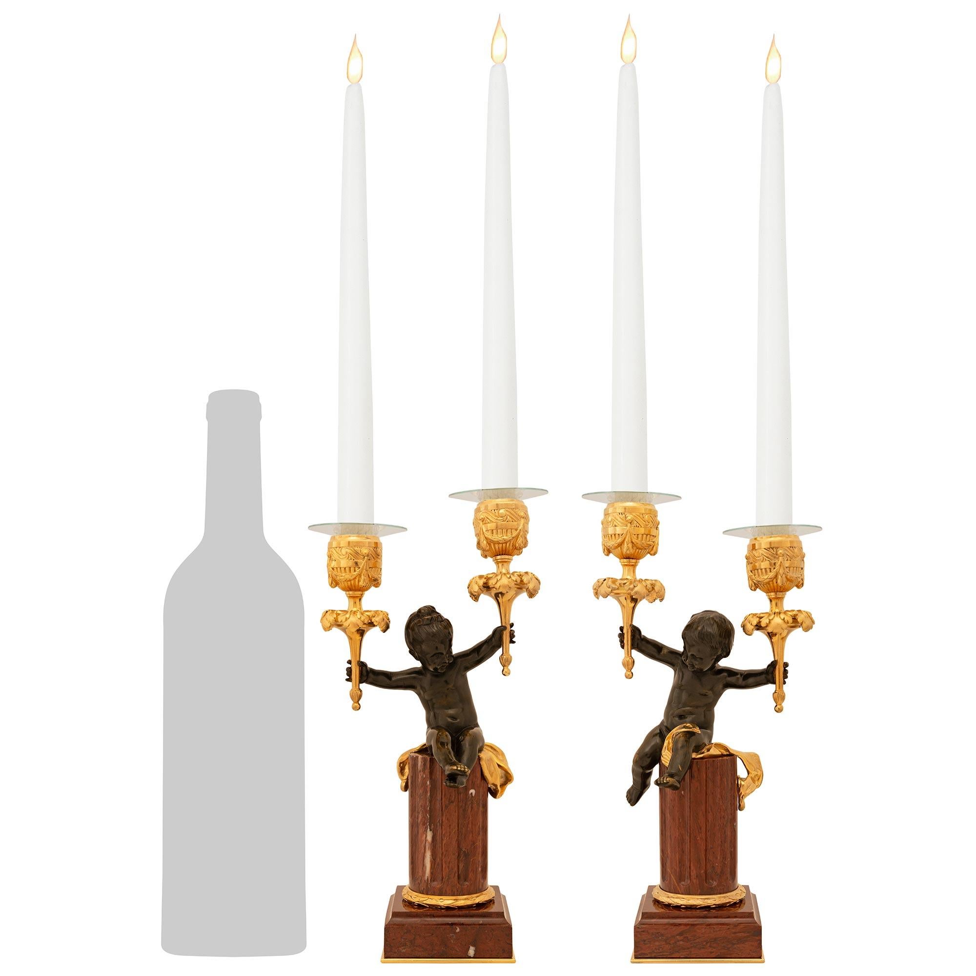 A high quality true pair of French 19th century Belle Époque period Louis XVI st. Rouge Griotte marble, patinated Bronze and Ormolu candelabras. Each exquisite two arm candelabra is raised by a Rouge Griotte marble pedestal and supported on a square