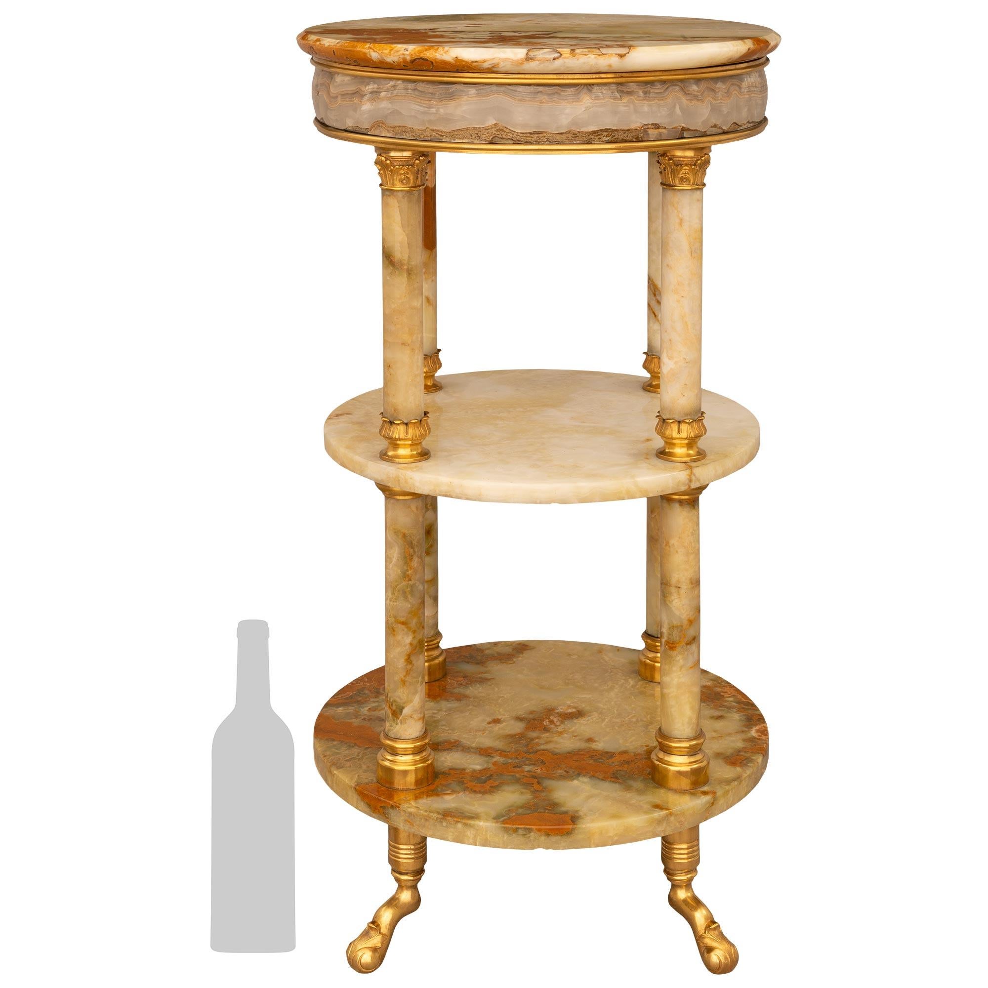 Superbe et très décorative table d'appoint en onyx et bronze doré d'époque Louis XVI, XIXe siècle, Belle Époque. Cette magnifique table d'appoint circulaire à trois niveaux repose sur quatre pieds angulaires décorés de feuilles d'acanthe enroulées.
