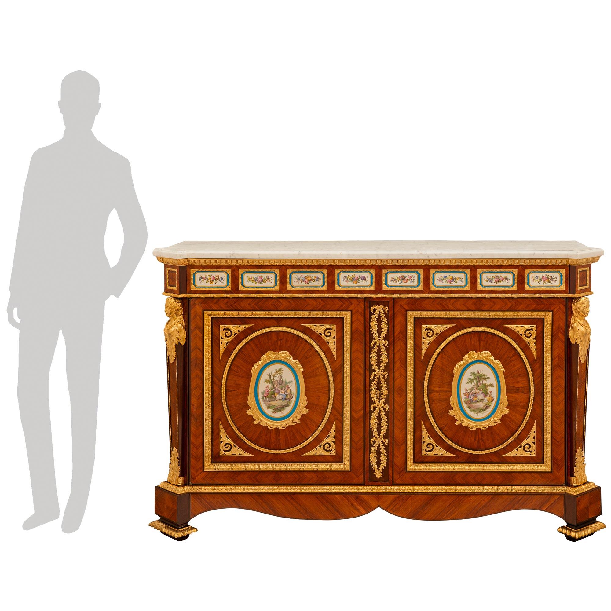 An impressive and exceptional quality French 19th century Belle Époque period Louis XVI st. Tulipwood, Kingwood, Sévres Porcelain, Ormolu, and white Carrara marble cabinet. This stunning cabinet is raised on square feet highlighted with fluted