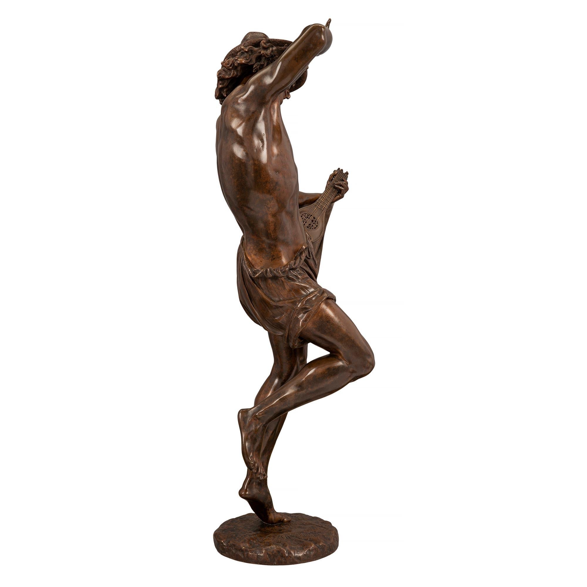 A stunning and high quality French 19th century Belle Époque period patinated bronze statue of a man dancing and playing a mandolin. The statue is raised by a circular base with a terrain design where the charming young man is dancing. He is wearing