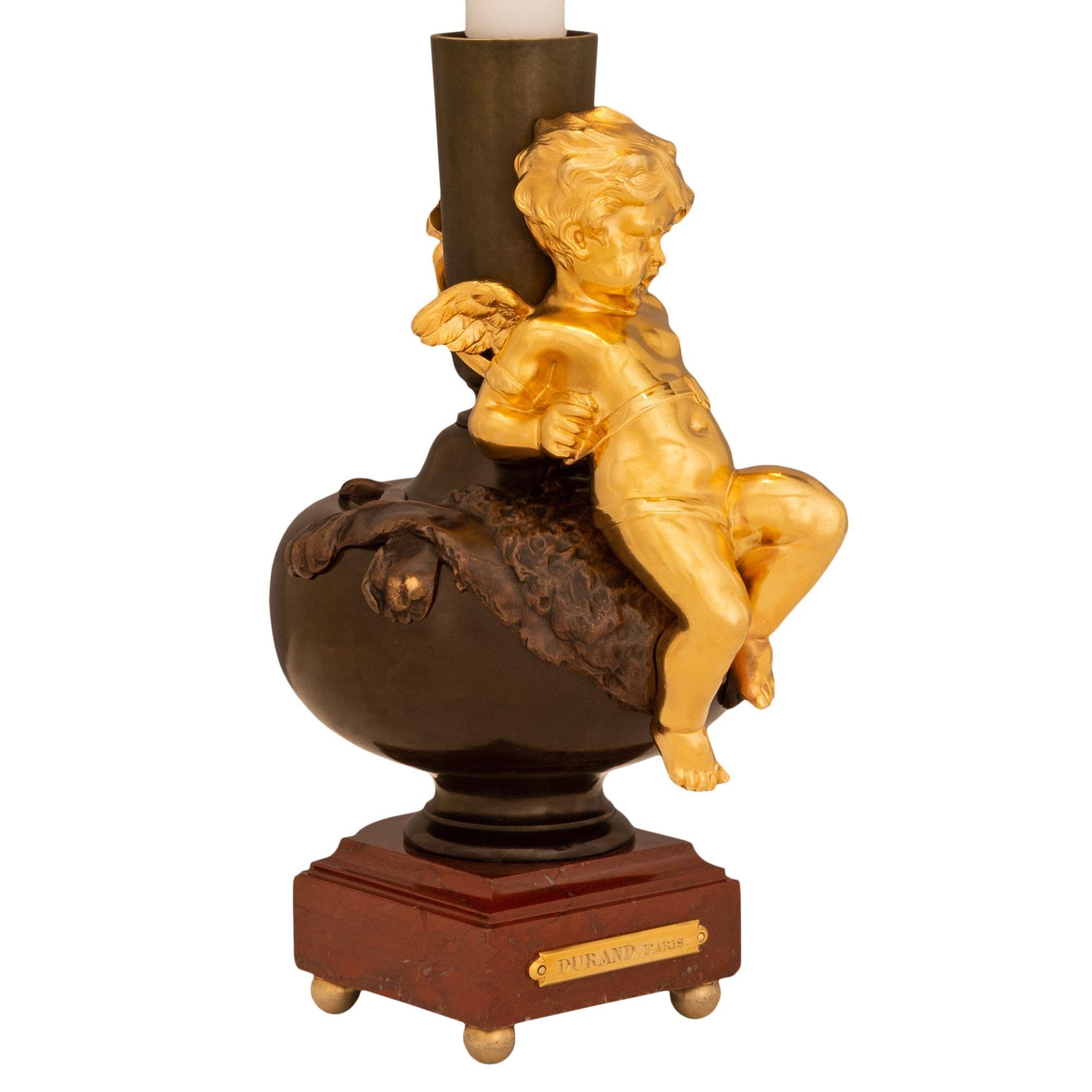 A small scale and most elegant French 19th century Belle Époque period Rouge Griotte marble, patinated Bronze, and Ormolu lamp, signed 'Durand, Paris'. This very decorative two light urn mounted into a lamp is raised by a square Rouge Griotte marble