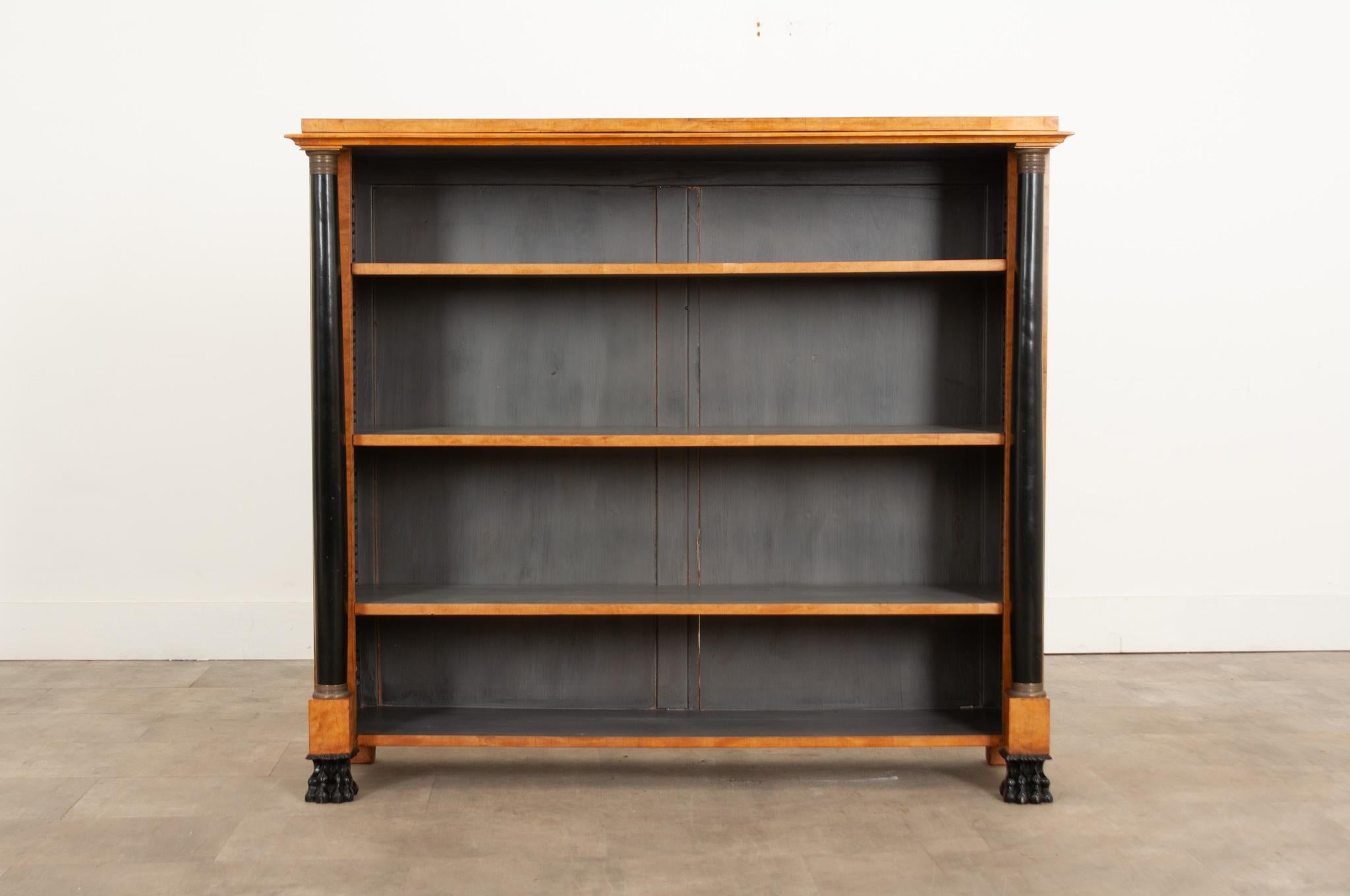 An early 19th century French Biedermeier polished satinwood bookcase with ebony accents. This attractive open bookcase, circa 1830 in date, has a stunning pair of ebonized columns with decorative brass capitelli encircled with neoclassical patterns