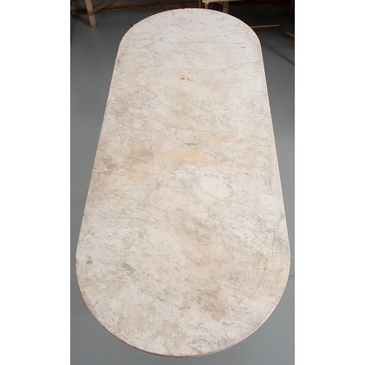 A classically styled, French bistro table. The table features a white capsule-shaped marble top resting on a cast iron base with X-form stretcher and more recent light blue paint. This piece shows some wear from being outside and it seats six