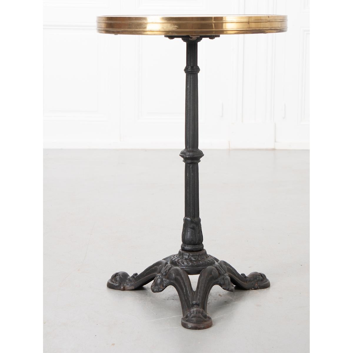 A classically styled French bistro table from the late 19th century. The table features a round white marble top that is encircled by a brilliantly-patinated wide brass band. The top is affixed to a cast iron tripodal pedestal base with feet