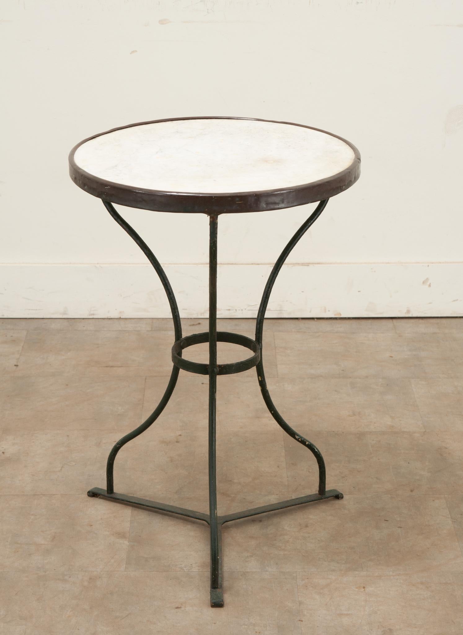 A classic Parisian style marble top & iron bistro table. The white marble top is surrounded by a tarnished brass band over three iron splayed legs. The patina and wear are consistent with age, be sure to view all the detailed images to see the