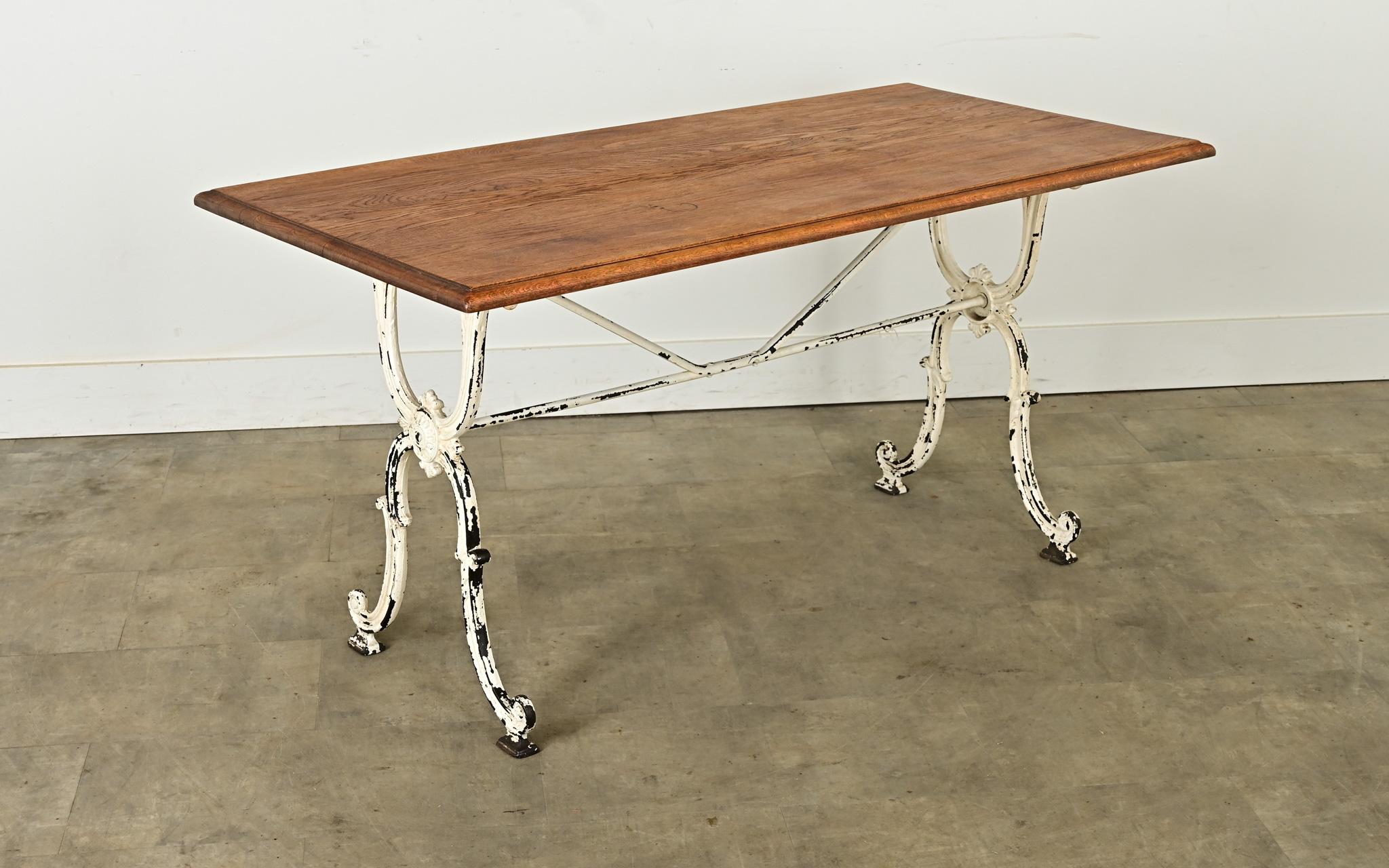 Mesa bistro francesa vintage con tablero de roble sobre base de hierro fundido del siglo XIX. Las planchas de roble tienen un color y un veteado preciosos, y están fresadas en los bordes para aportar una sutil sofisticación. La pátina del tablero de