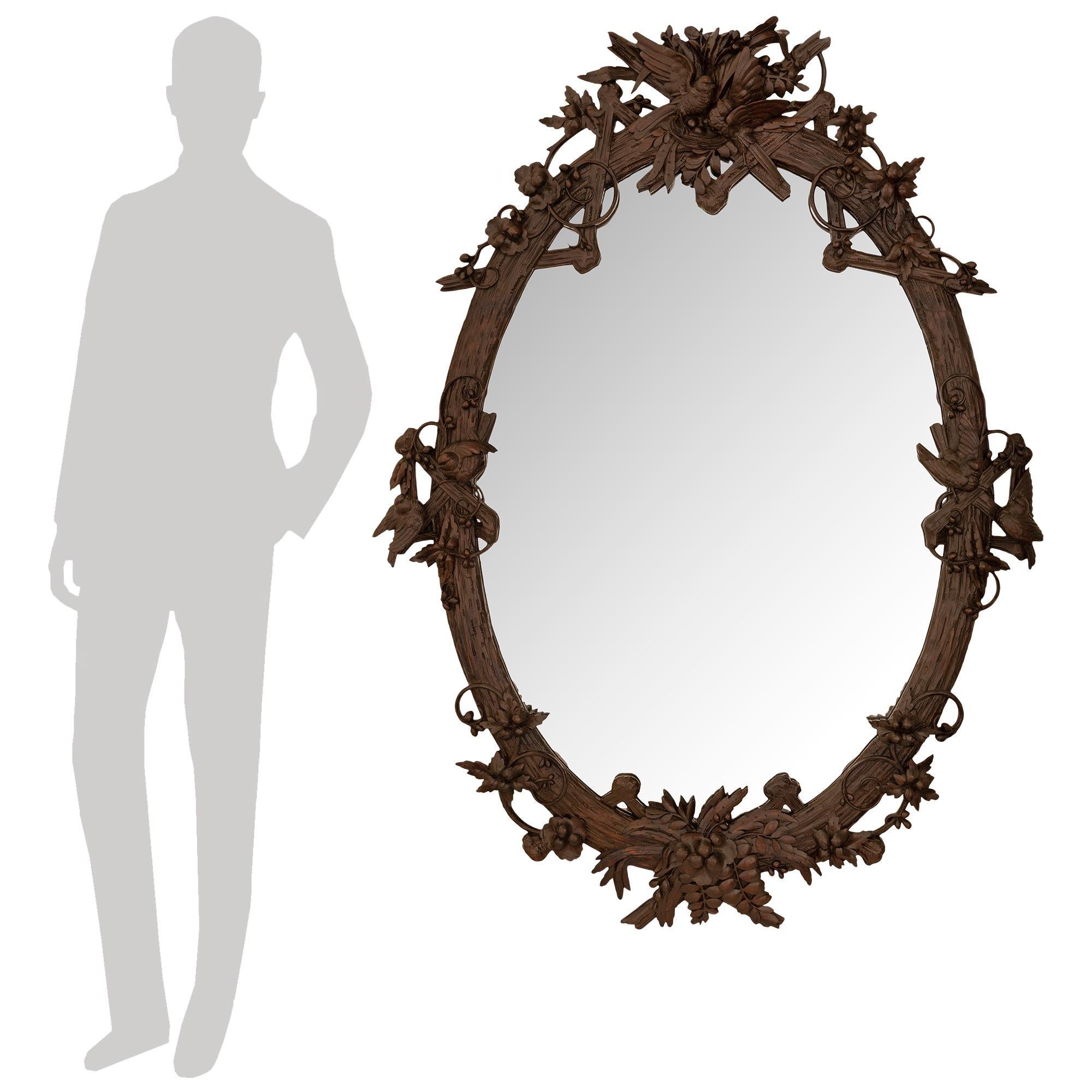 A unique and most handsome French 19th century Black Forest st. Walnut mirror. This stunning oval Black Forest mirror with its original mirror plate is wonderfully decorated by berried floral designs and birds. The top crown is decorated with an