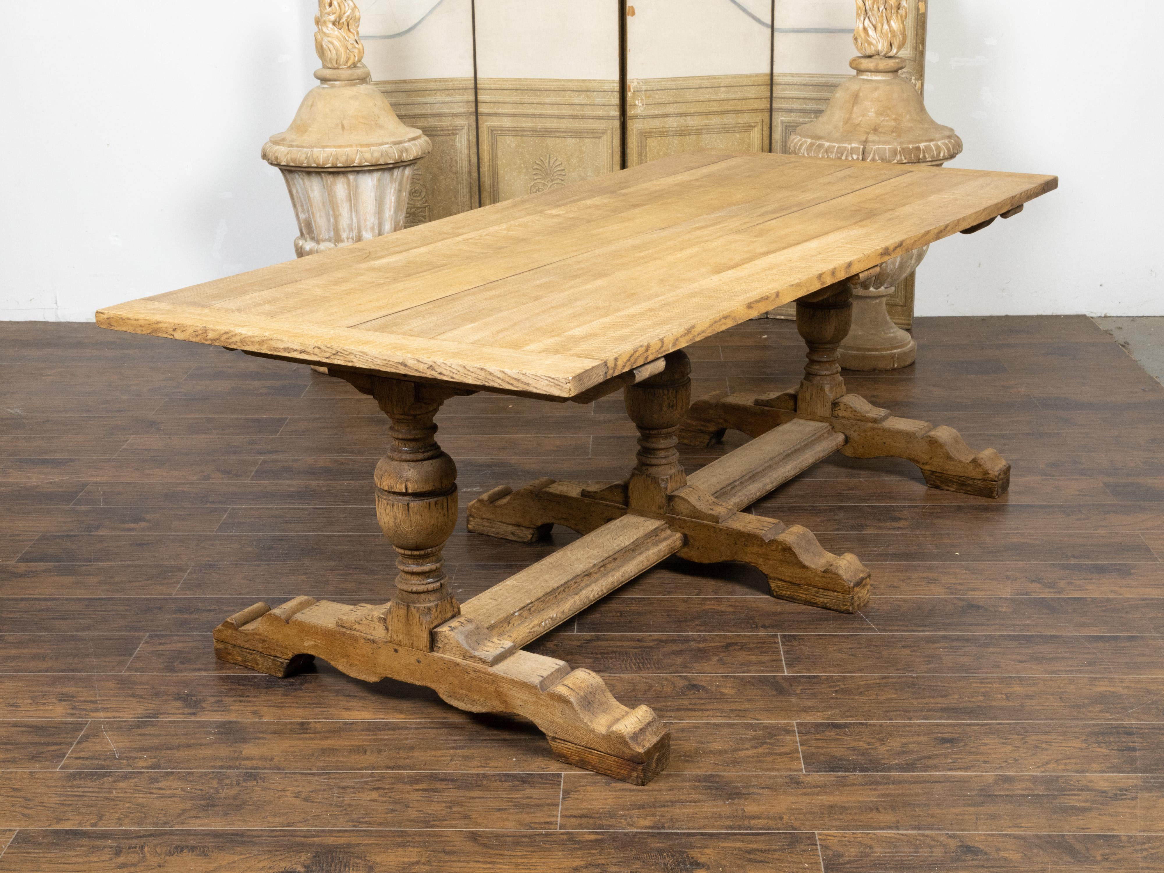 A French bleached oak farm table from the 19th century, with trestle base, baluster legs and weathered patina. Created in France during the 19th century, this bleached oak farm table features a rectangular planked top sitting above an elegant