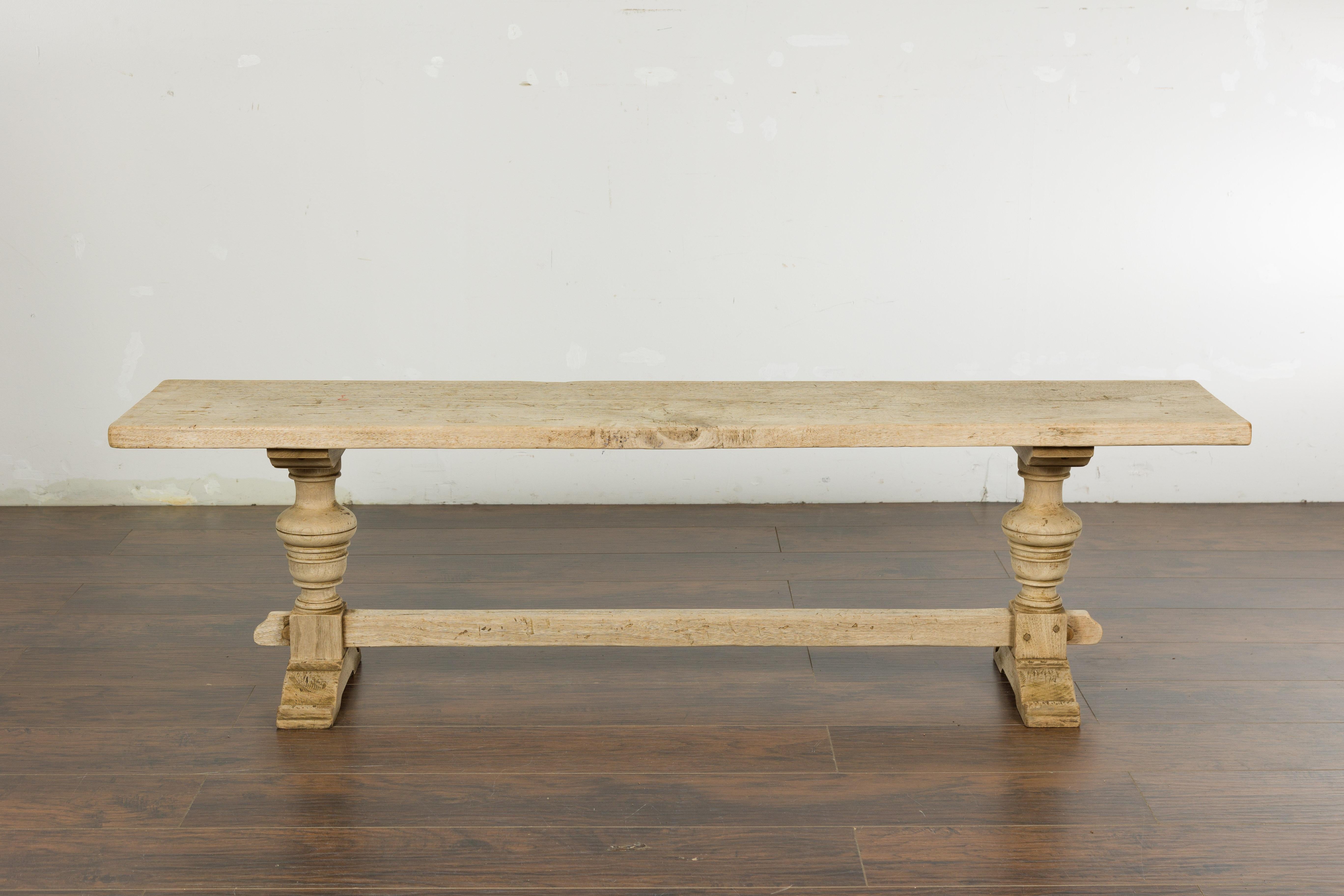 A French bleached walnut bench from the 19th century with trestle base made of two turned baluster legs connected to one another through a plain cross stretcher. Emanating a harmonious blend of rustic allure and timeless elegance, this 19th-century