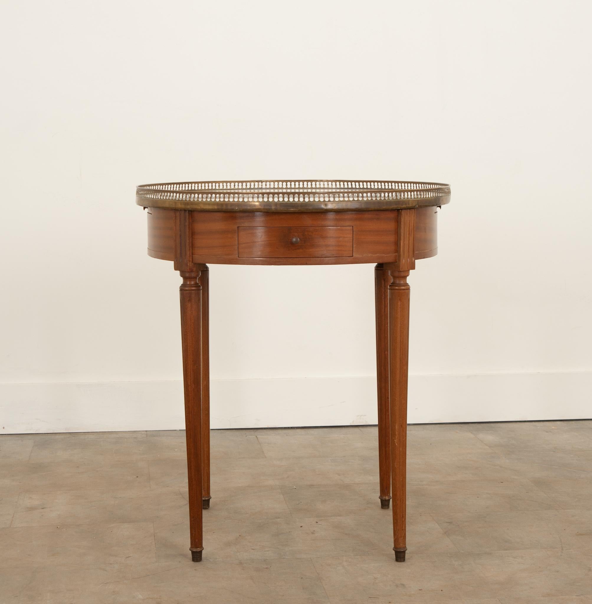 A charming French mahogany gueridon bouillotte table originally used for playing cards. Topped with white marble and surrounded by a pierced brass gallery that’s nicely patinated. Two drawers and two slides are housed within the apron, all with