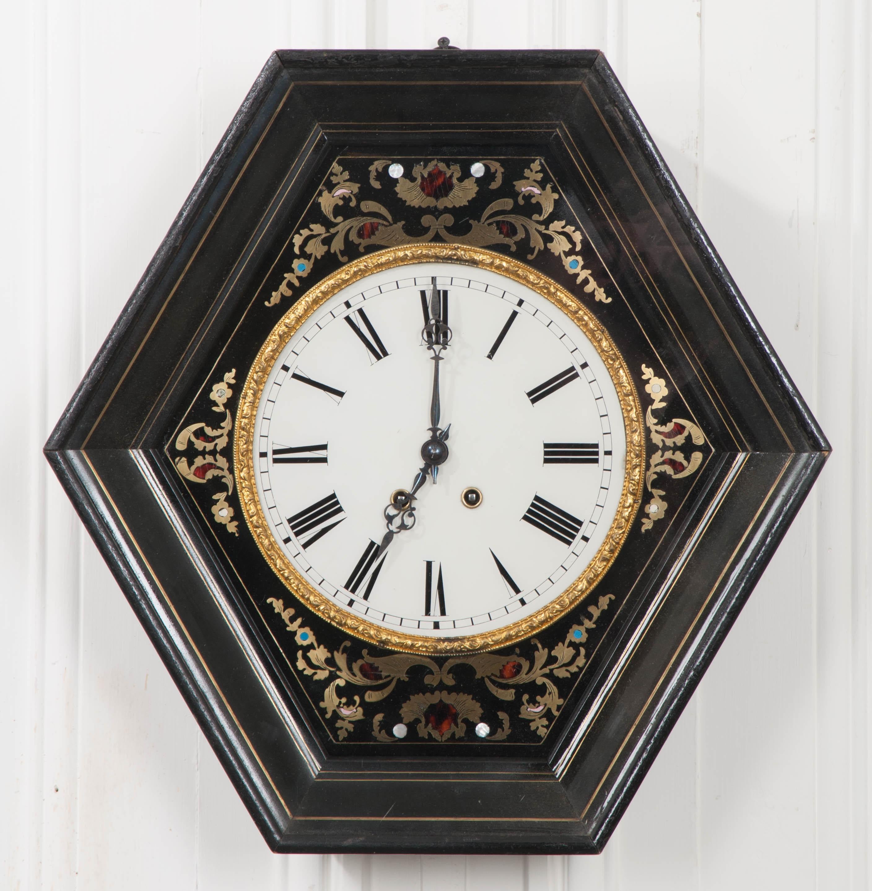 This stunning French 19th century Boulle-work brass, tortoiseshell, and mother of pearl inlaid wall clock is in working condition with the original parts. The mahogany and brass line-inlaid hexagonal frame retains its original wavy glass. The