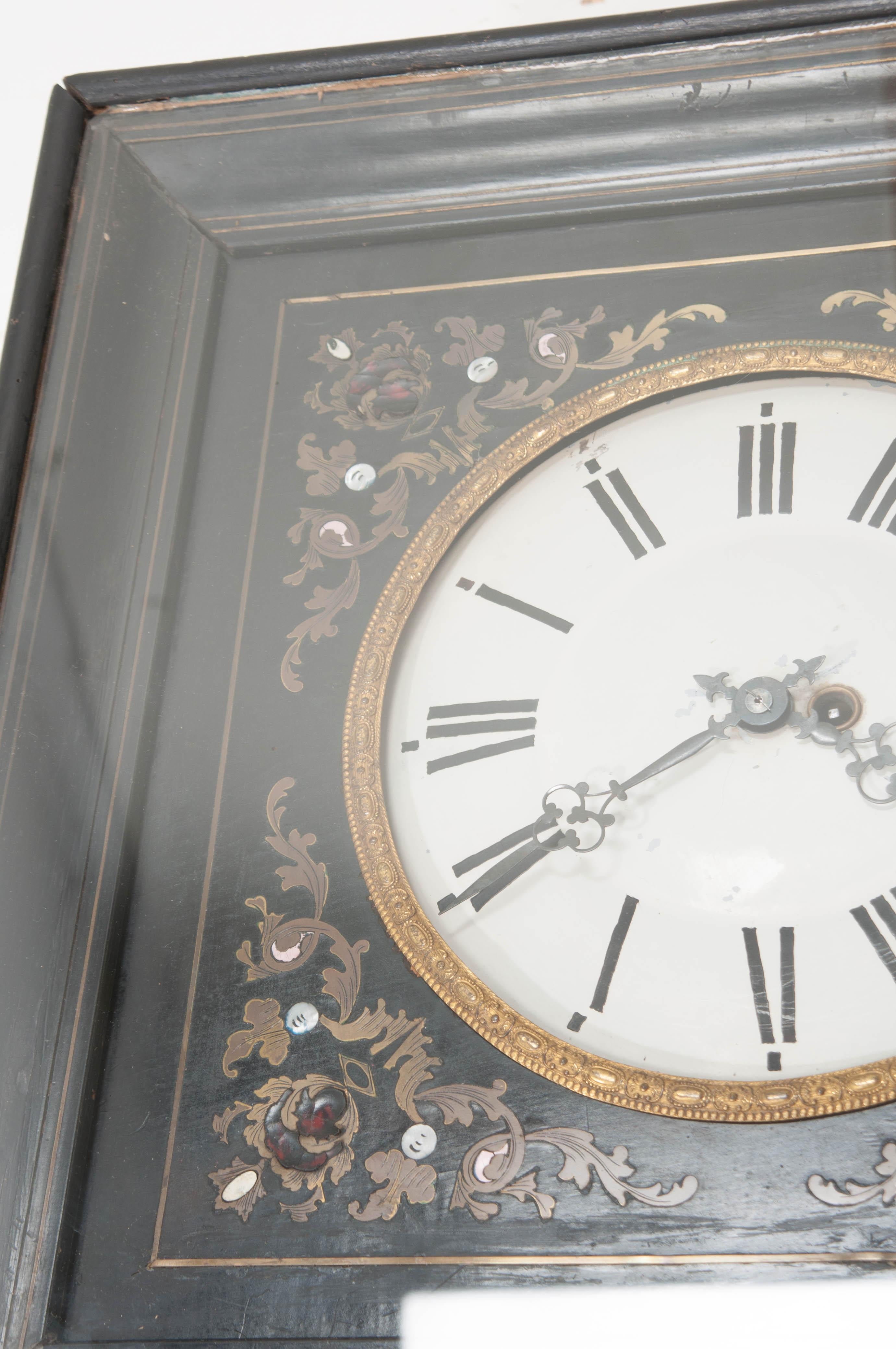 This fine Boulle-inlaid and ebonized wall clock, circa 1870, features delicate scrolling inlays of brass, tortoiseshell, and mother-of-pearl surrounding a dial with hand-painted Roman numerals within an ormolu bezel. It is presented in the original