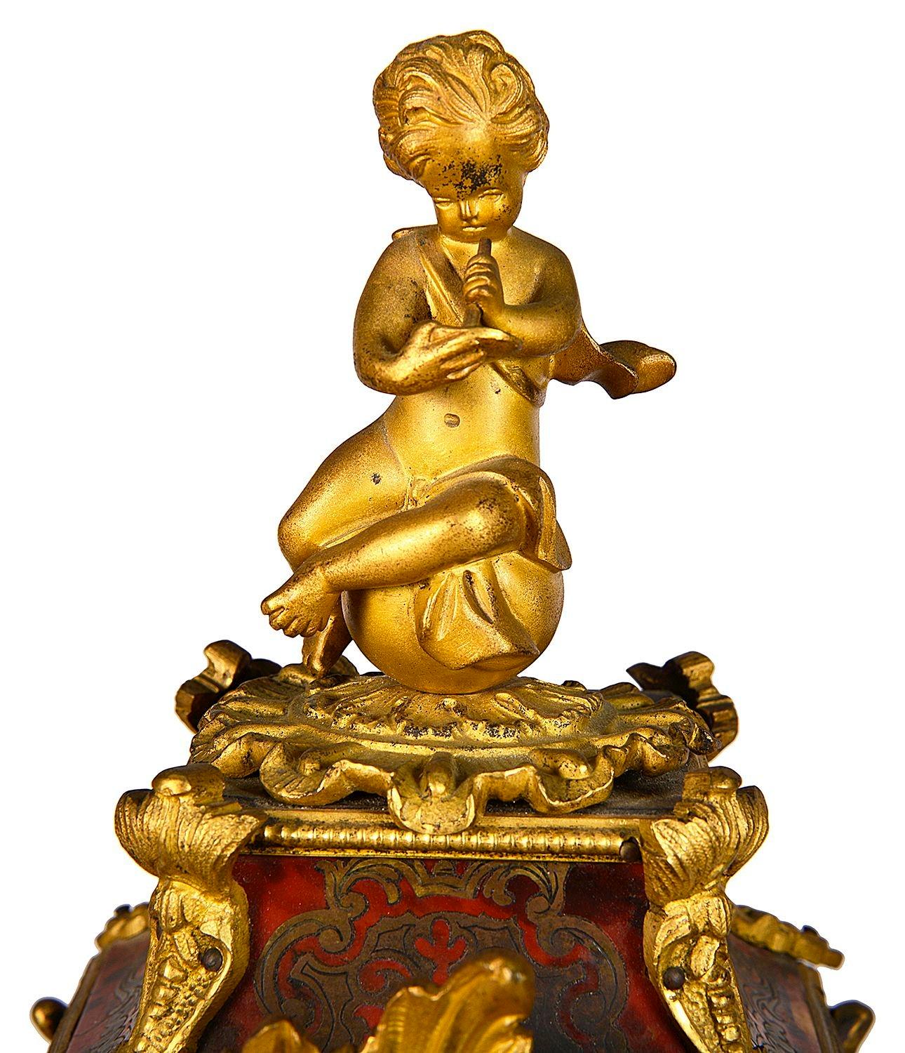 A very good quality French 19th Century Boulle mantle clock, having a gilded ormolu putti seated on the top, Red tortoiseshell and brass inlay to the serpentine shaped case, wonderful gilded rococo style ormolu mounts and feet. The white and blue