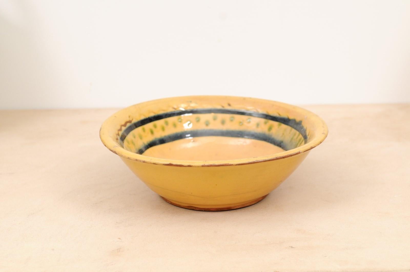 A French 19th century pottery bowl from the Poterie Hertz in Annecy, with yellow glaze. Created in the Alpine town of Annecy in Southeastern France, this pottery bowl features a circular yellow glazed body adorned with black, green and brown motifs.