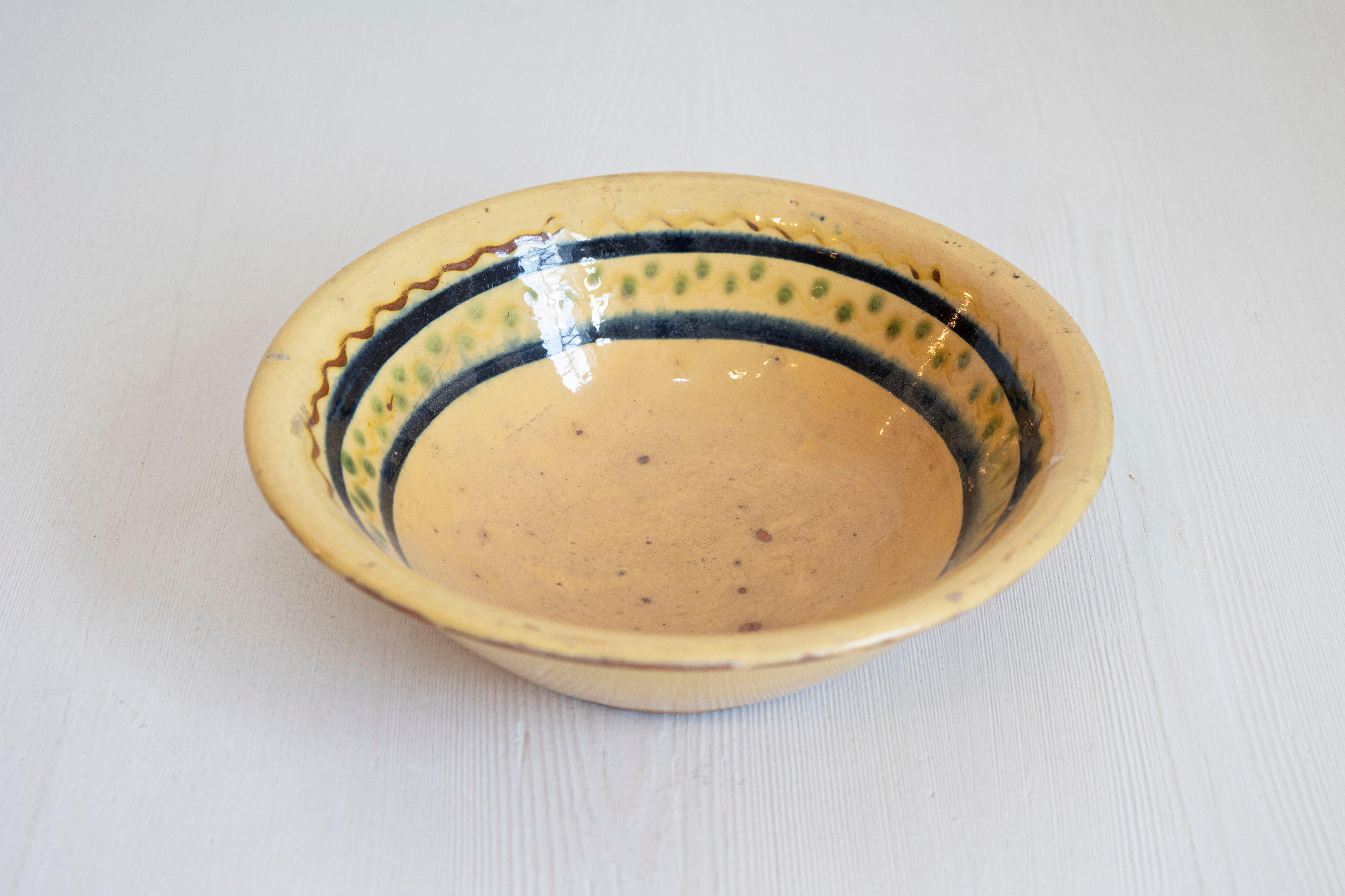 A French 19th century pottery bowl from the Poterie Hertz in Annecy, with yellow glaze. Created in the Alpine town of Annecy in Southeastern France, this pottery bowl features a circular yellow glazed body adorned with black, green and brown motifs.