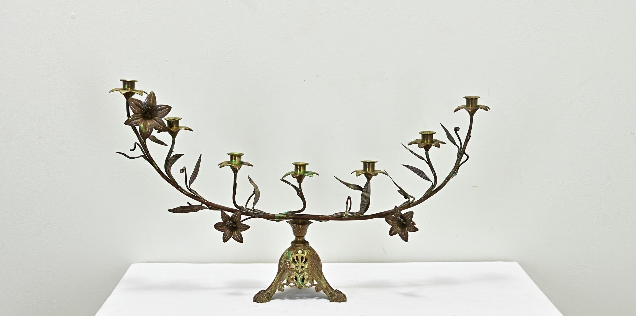 A large French seven light gilt brass candelabra from the 1800’s. This whimsical fixture from a church has seven candle cups and gilt bronze flowers. The tripod base has three legs with religious motifs, leaves and berries. Patina consistent with