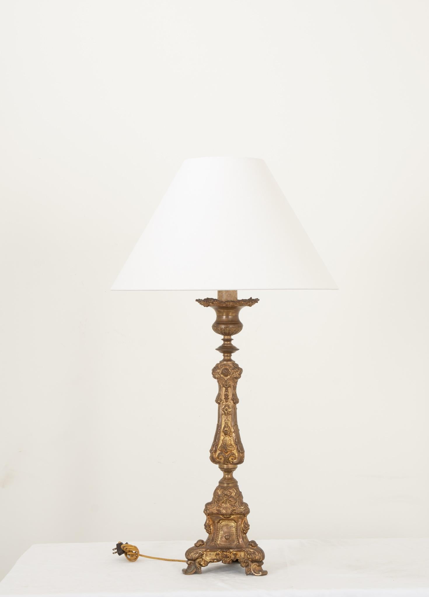 Un antico candeliere da altare in ottone del XIX secolo in Francia, trasformato in una lampada elettrificata. Questo splendido apparecchio è molto decorato con dettagli decorativi su ogni superficie. La lampada poggia su tre piedini a voluta. L'arpa