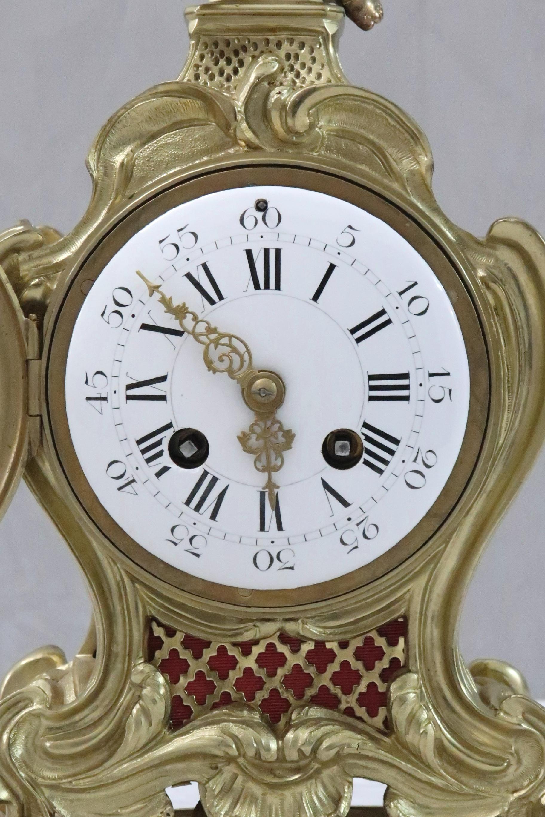 An excellent quality French 19th century serpentine shaped brass and gilt Rococo style mantel clock on stand with floral leaf decoration and cherub finial. The clock has a white enamel dial with a French eight day movement with outside count wheel