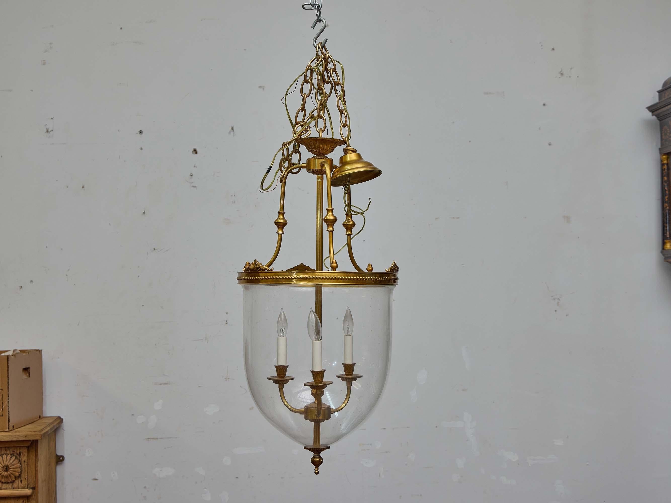 This elegant French brass and glass bell jar lantern dates to the 19th century and embodies the restrained refinement of neoclassical lighting from the period. The fixture features a gracefully curved, hand-blown glass dome suspended from a finely