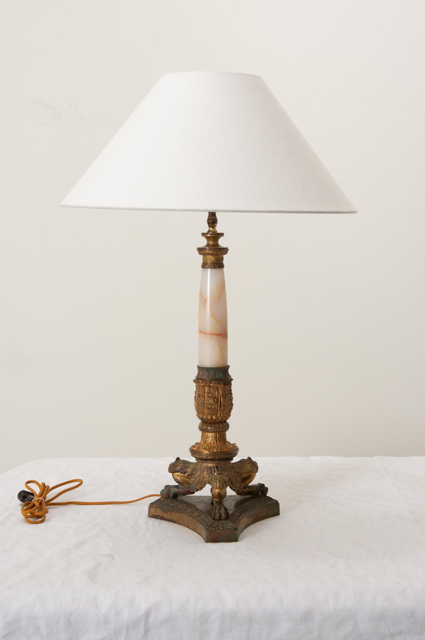 A 19th century French Empire style single light table lamp with contemporary linen shade. Elegant with neoclassical designs and featuring a tapered onyx shaft ornamented with decorative brass mounts supported by a wonderful triform lion paw footed