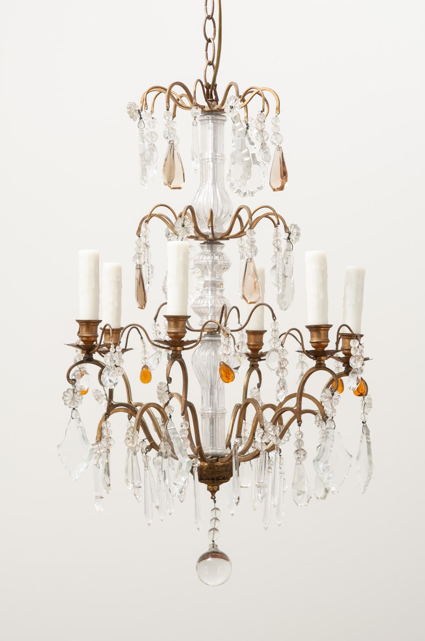 An elegant 6-light brass and crystal chandelier made in France. This chandelier has a brass frame with cut crystal drops hanging from its curving arms. There are six lights each with faux candle covers. This light fixture has been cleaned and wired