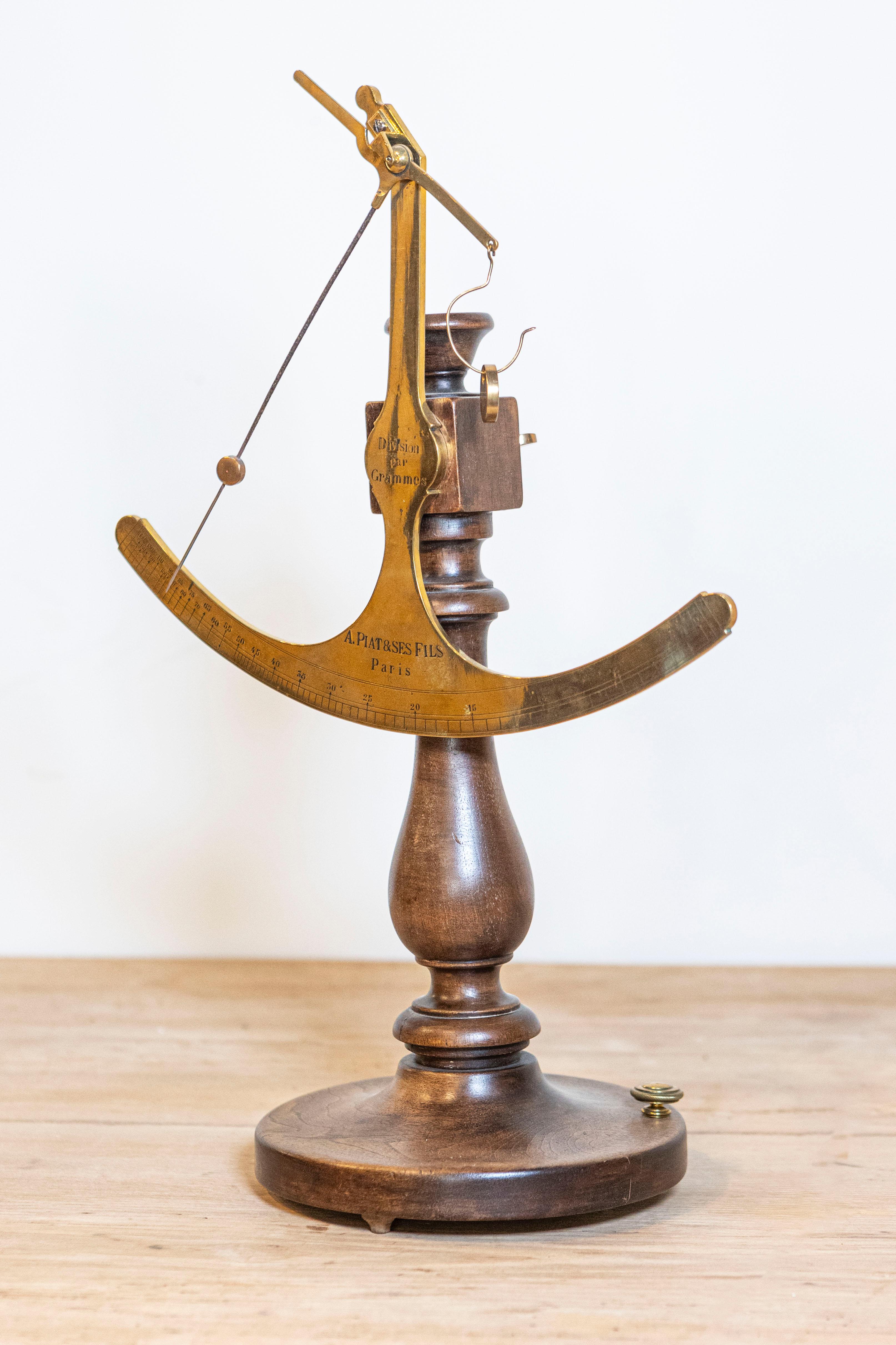 Balance à tissu en laiton du 19e siècle, avec base en bois, provenant de la Maison Piat. Créée à Paris au XIXe siècle, cette balance à tissu, en laiton, est montée sur un socle circulaire en bois tourné. Signé A. Piat & ses Fils (A. Piat and Sons)