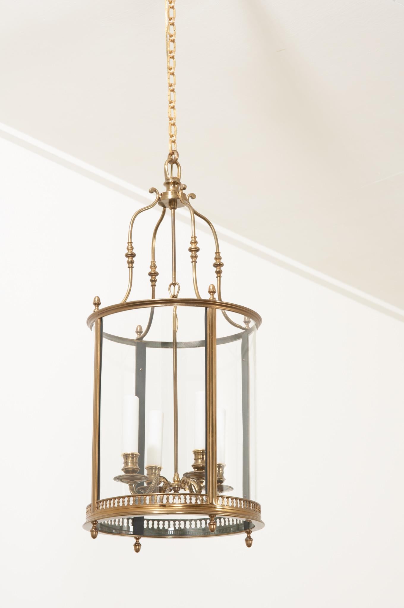 This medium sized brass and glass lantern is perfect wherever a single fixture is needed. A simple 5” diameter canopy sits flush to the ceiling and connects to a classic brass chain to support the whole. Four scrolling arch-forms hook onto the