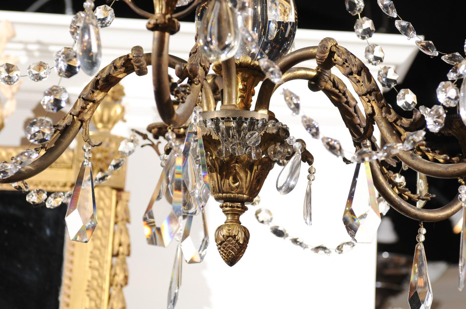 A French crystal and bronze 10-light tiered chandelier from the 19th century, with large crystal stem and scrolling arms. Born in France during the 19th century, this exquisite chandelier features a central stem, draped with petite faceted crystals