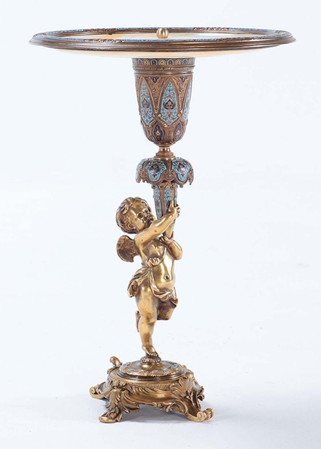 Dieser französische Tafelaufsatz aus dem 19. Jahrhundert zeigt die bemerkenswerte Kunstfertigkeit der Champlevé-Bronze in Kombination mit der Eleganz des Onyx. Das Mittelstück ist mit einer beeindruckenden Onyxplatte versehen, die der