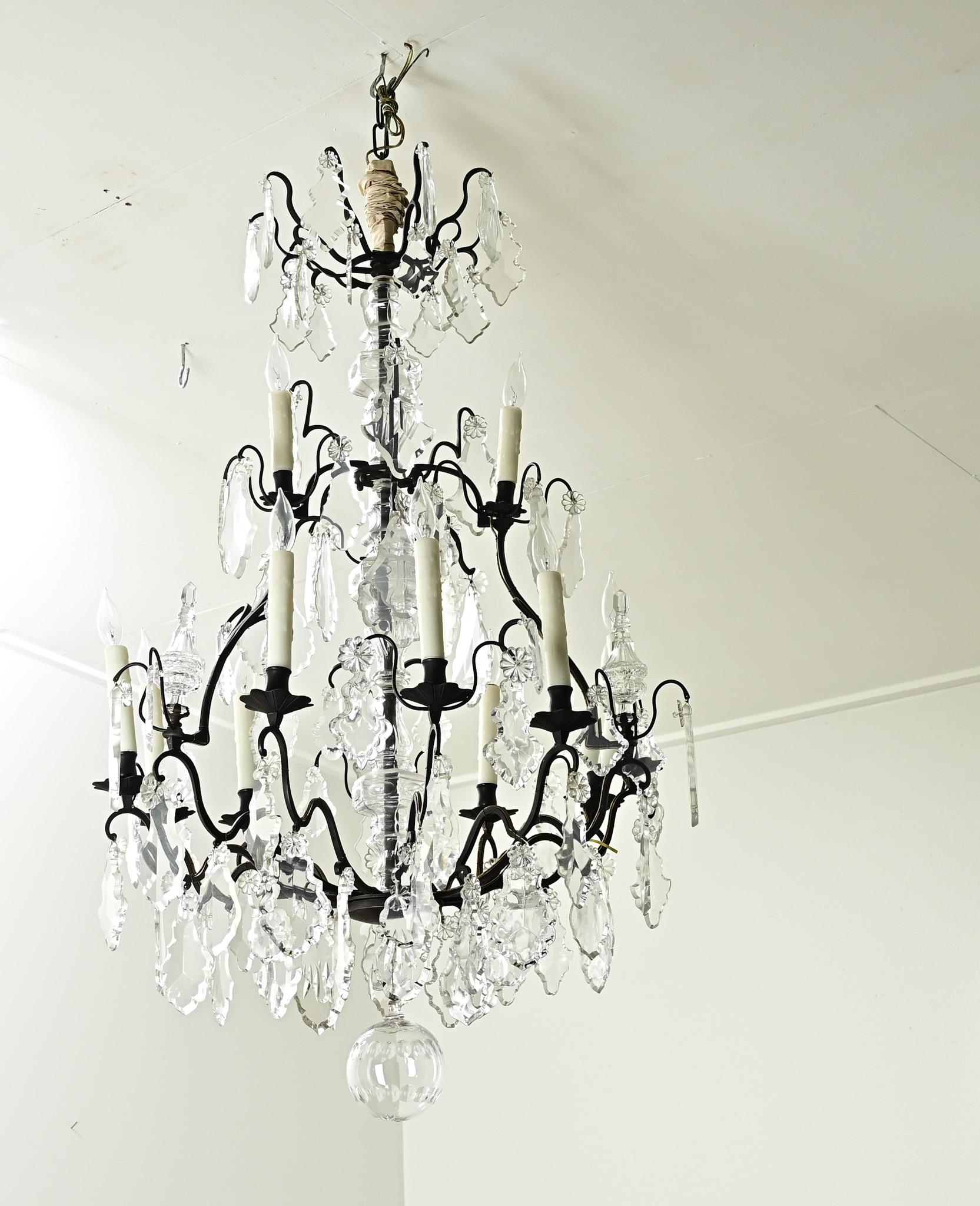 A large French twelve light bronze and crystal chandelier from the 1800’s. This statement chandelier has a bronze frame with cut crystal drops and cut crystal floral designs hanging from twelve scalloped chandelier arms with faux wax candle covers.