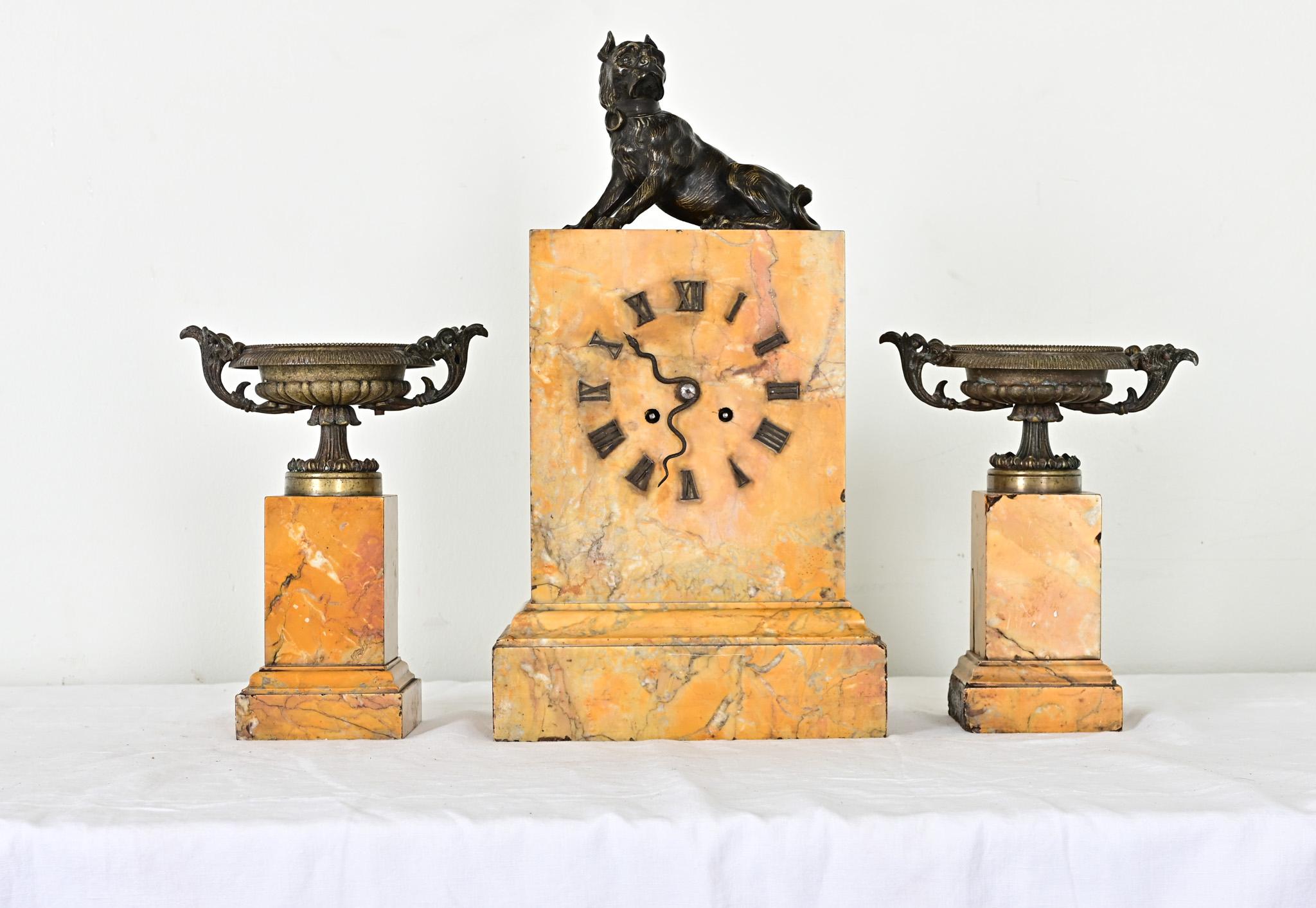 Stunning three-piece mantel clock set in Siena marble and bronze, French Empire period. The main piece at center features a cast bronze hound sitting uneasily upon the plinth. Roman numerals are applied directly to the marble face in lieu of a dial,