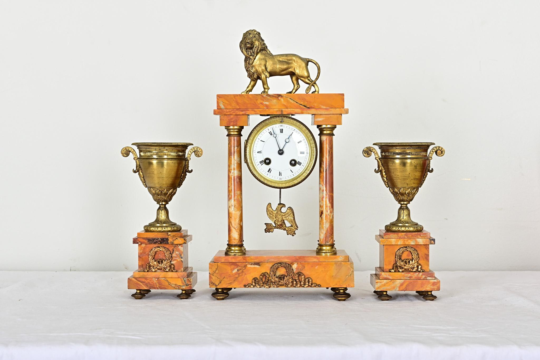 A captivating three-piece mantel clock, from 19th century France, crafted in Siena marble and gilt bronze, with multiple stylistic reference points from the Grand Tour of Europe. The architectural clock tower at center features a cast bronze lion