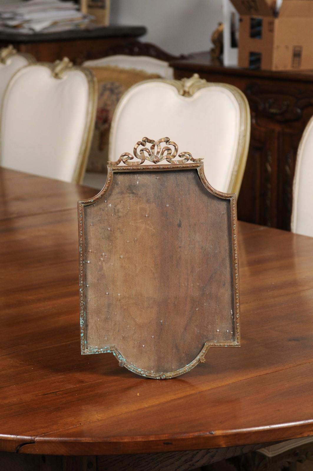 A French bronze picture frame from the 19th century, with bow motif. Created in France during the 19th century, this bronze piece is adorned with a delicate bow on the crest, sitting on a rectangular frame with in-curving accents in the upper