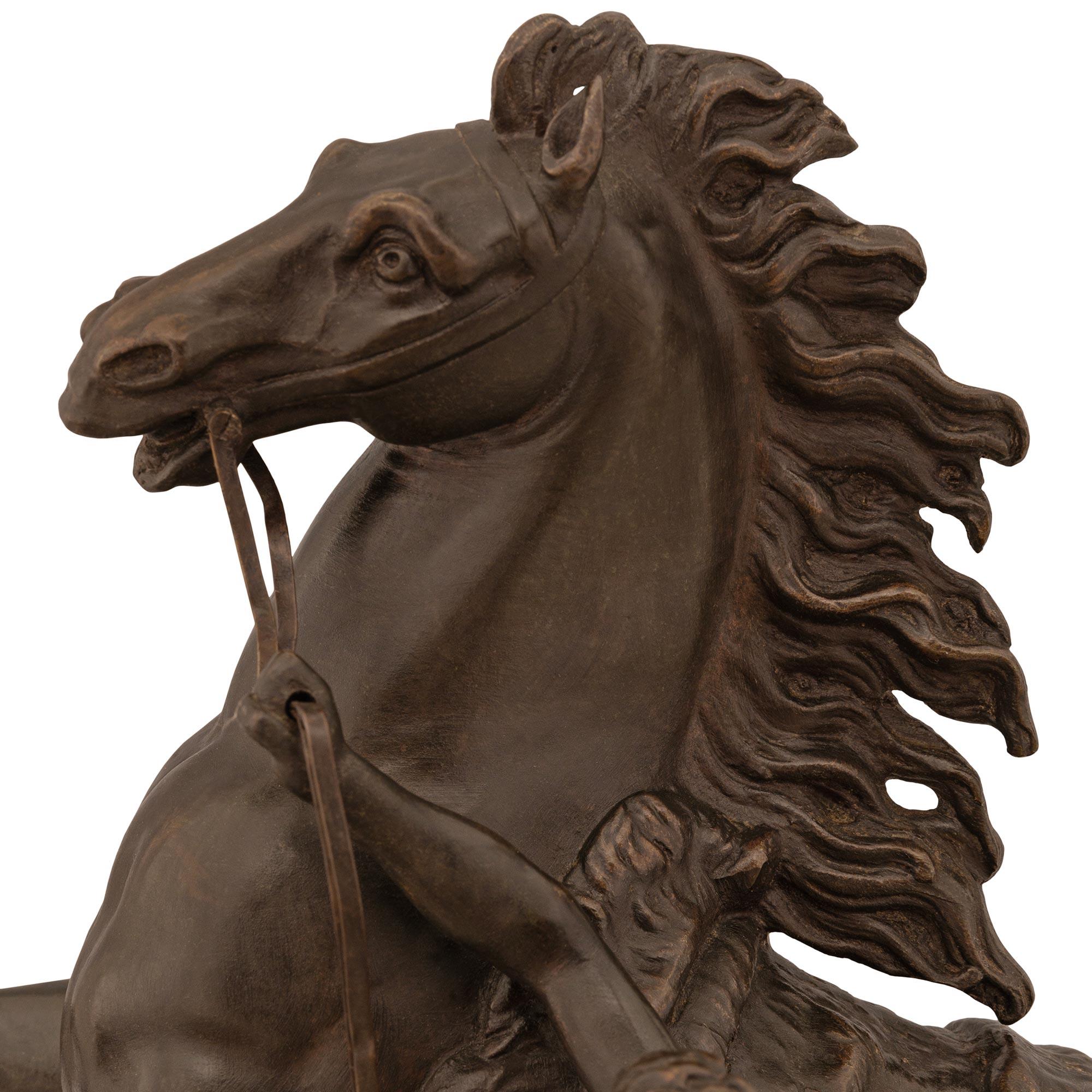 A handsome French 19th century patinated Bronze statue of a horse and groom, modeled after the horses of Marly. The spectacular horse is draped in a saddle blanket and displays a wonderful flowing mane and tail while rearing and being handled by a