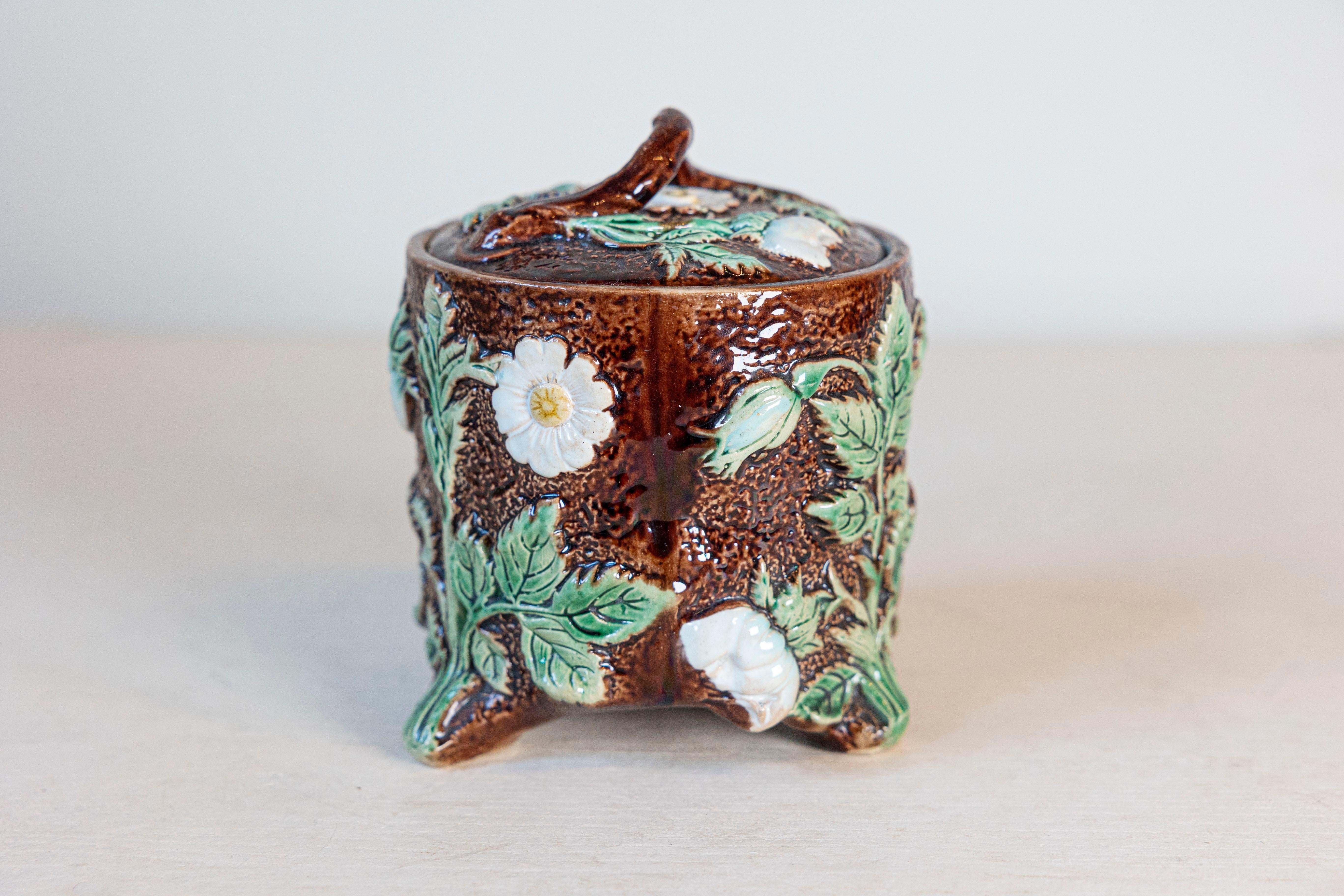Un vaso con coperchio in maiolica marrone francese del XIX secolo con decorazioni floreali verdi e bianche. Nato in Francia durante il XIX secolo, questo vaso in maiolica vanta un bel fondo marrone ornato da fiori delicatamente modellati di colore