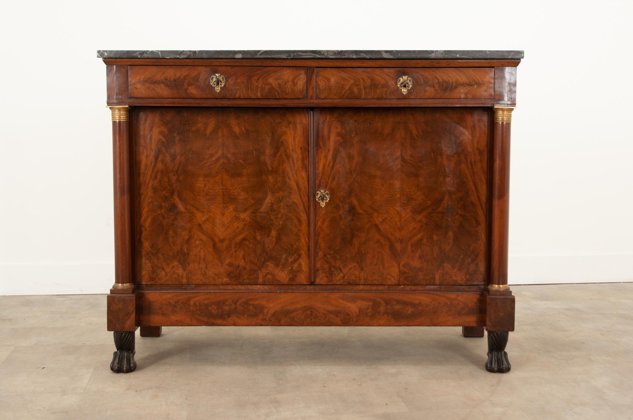 A French Empire buffet hand-crafted in France in the 19th century that features fabulous mahogany burl wood and neoclassical details. The original marble top is stunning with gorgeous dramatic patterns in the stone. The apron houses two drawers