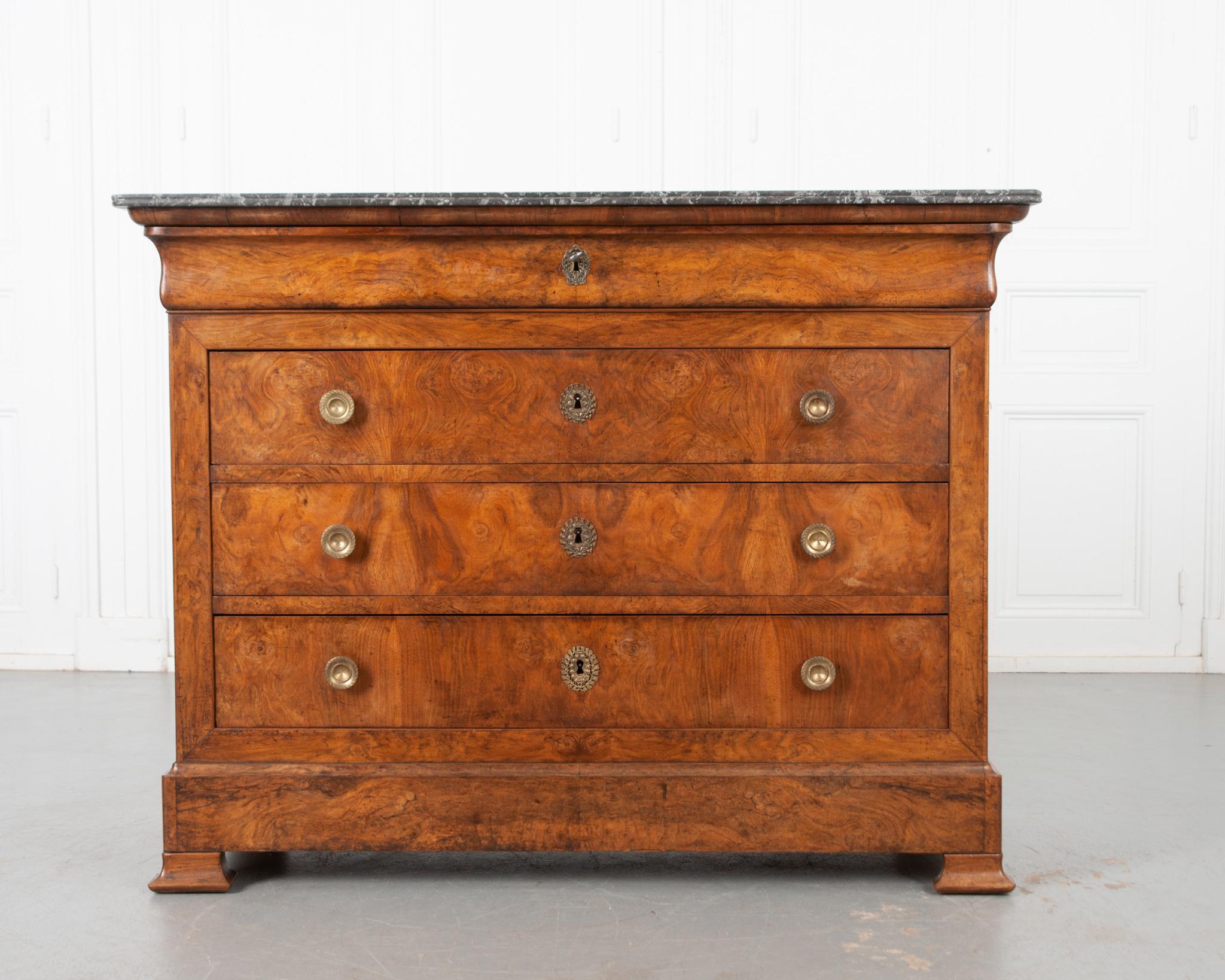 Gorgeous burl walnut was selected to finish the facade of this outstanding French Louis Philippe commode from the 19th century. A beautiful black and gray marble top sits atop the body, with a few surface scratches extant and a chip to the front