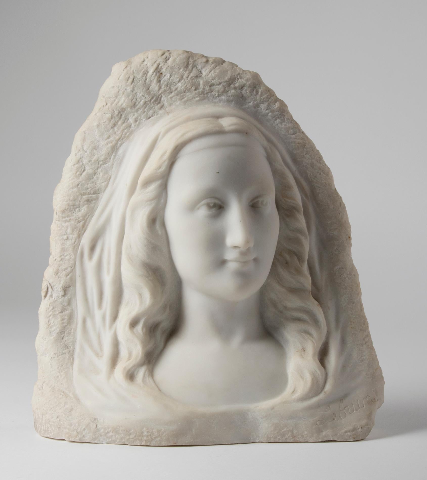 Beautiful marble statue, a portrait of a young woman, cut from Carrara marble. The statue has a beautiful artistic look. The woman's refined, serene face contrasts beautifully with the rough, unprocessed background of the Carrara marble. It is a