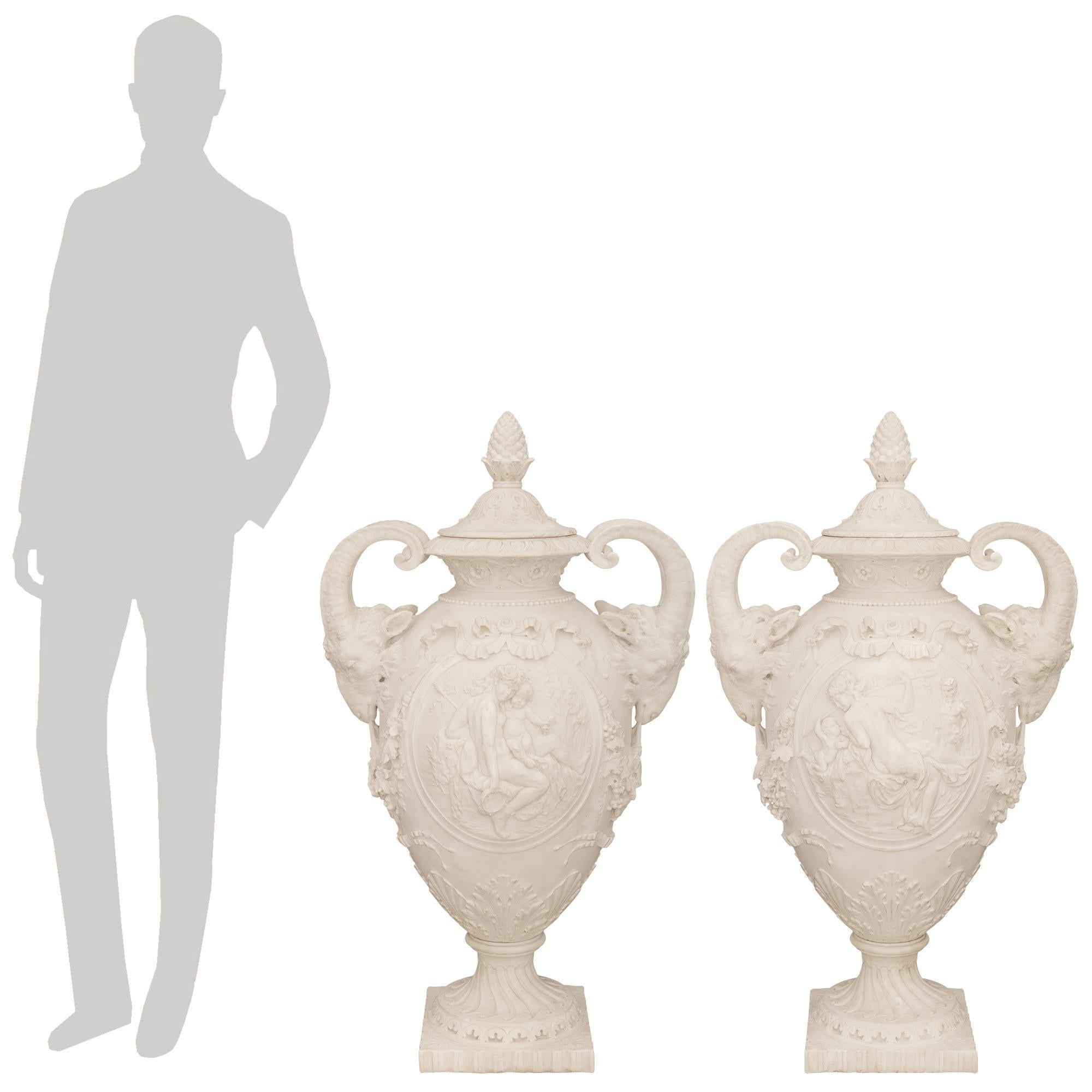 An exceptional and monumentally scaled pair of French 19th century Louis XVI st. White Carrara Marble urns, signed D. Epinay, Charles Adrien Prosper. Each stunning lidded urn is raised on a square carved base with a scalloped edges and flowers at